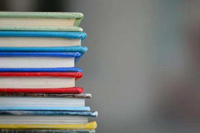 A stack of colorful books on a plain surface against a gray background.