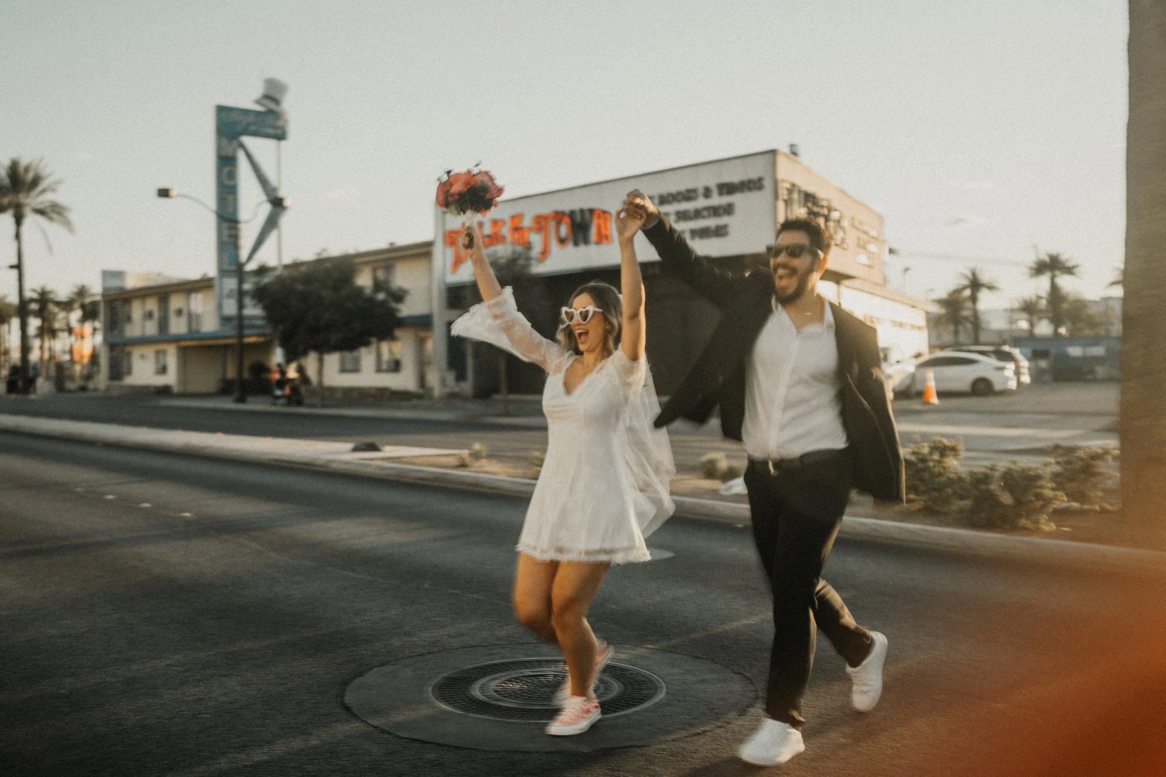Szczęśliwa para młoda biegnąca ulicą Las Vegas trzymając się za ręce po ceremonii ślubnej, golden hour