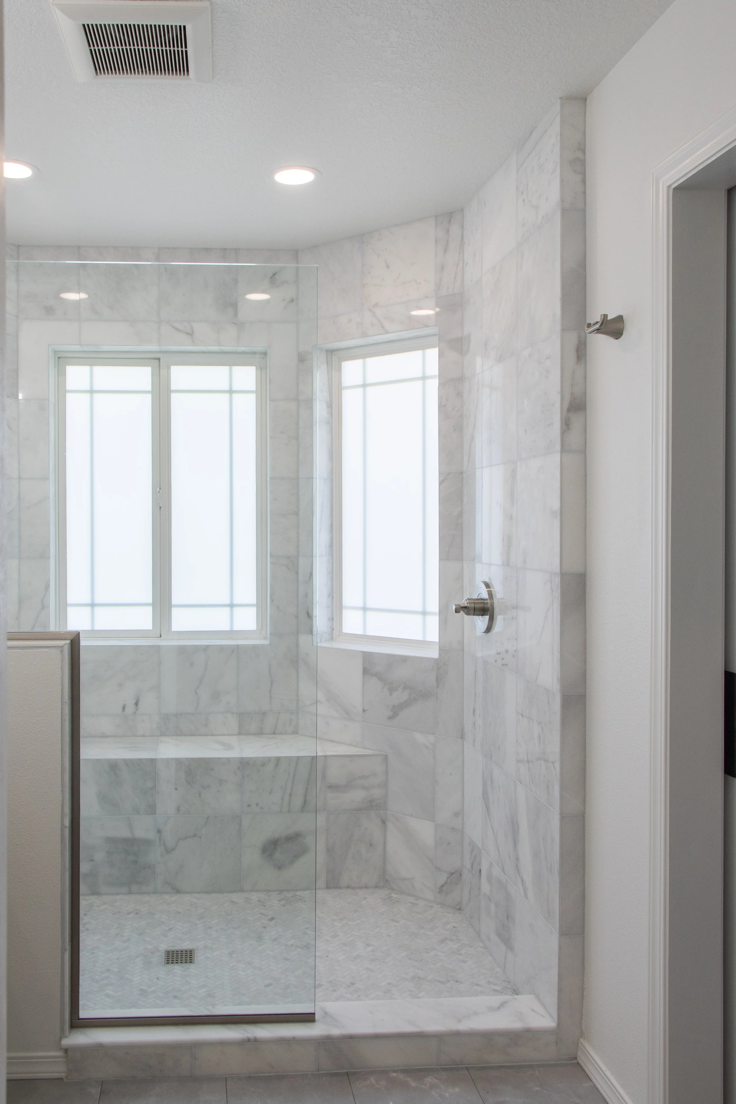 Marble walk-in shower with glass door, two windows, and ceiling lights in a modern bathroom.