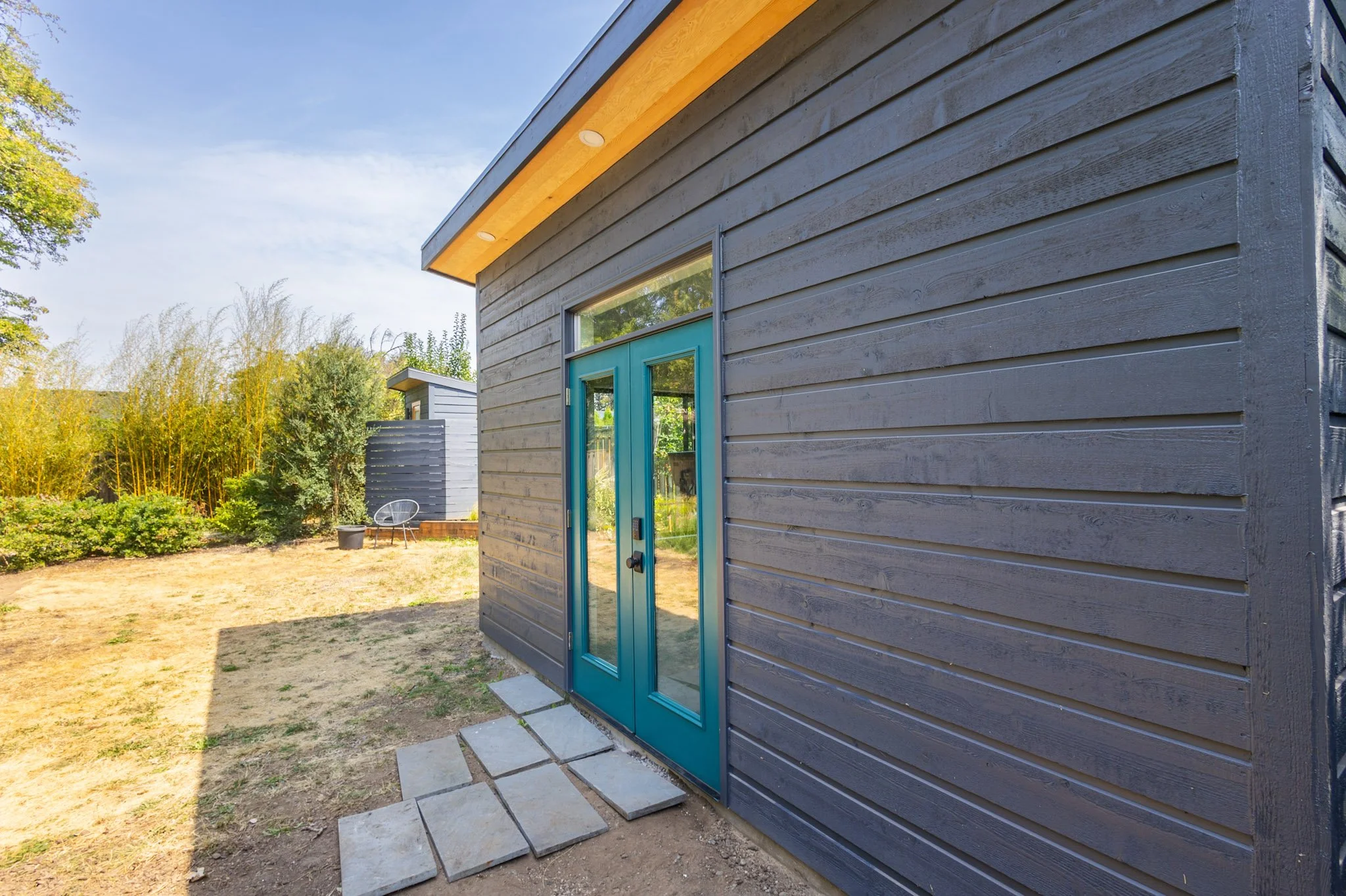 Side view of a new build ADU with black paint on the wood siding and a teal blue french door.