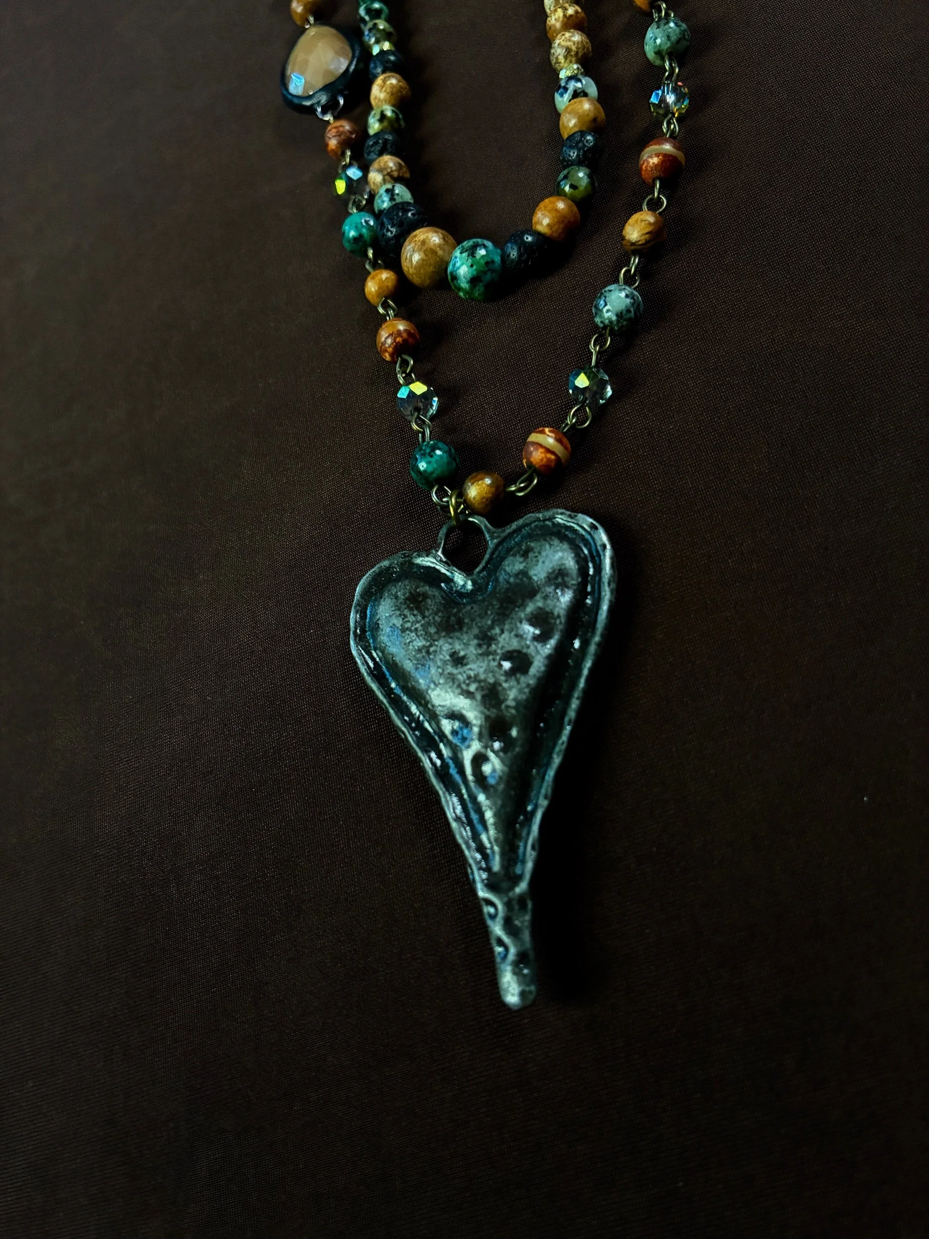 Moss Cathedral statement necklace displayed against dark fabric with its three strands arranged fully.