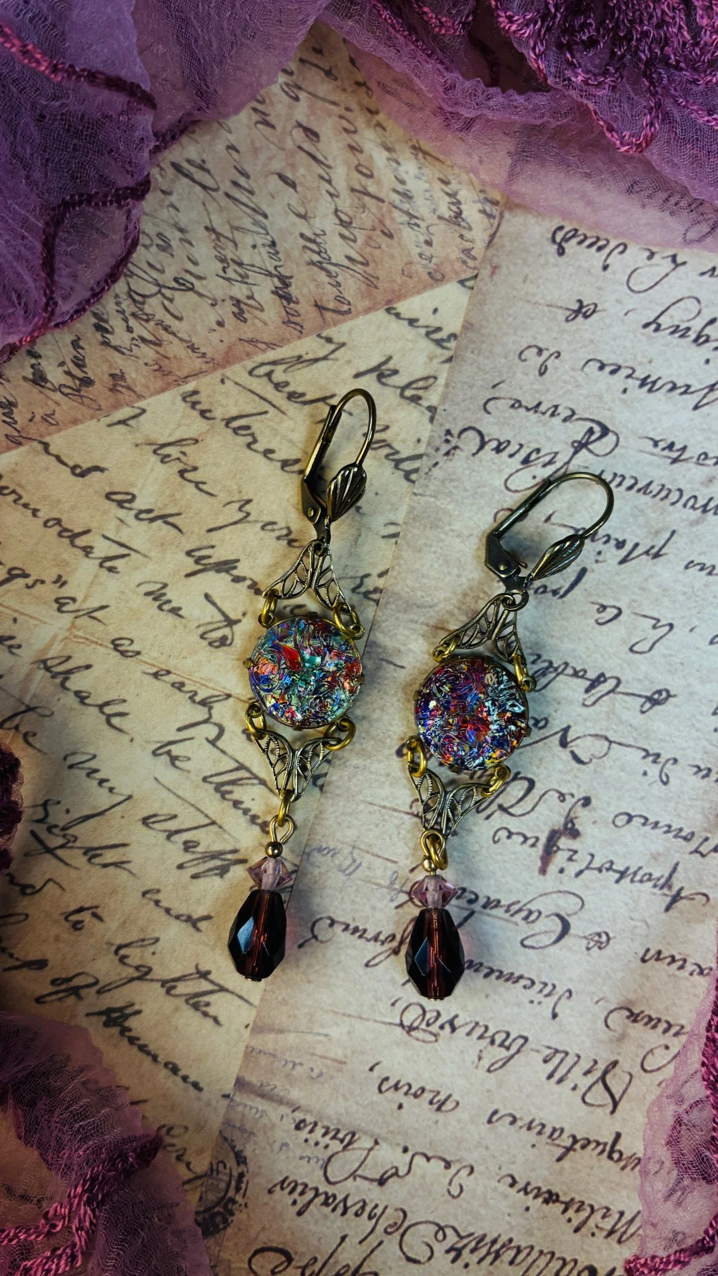 Long antiqued-brass Velvet Reverie earrings displayed against vintage-inspired fabric.