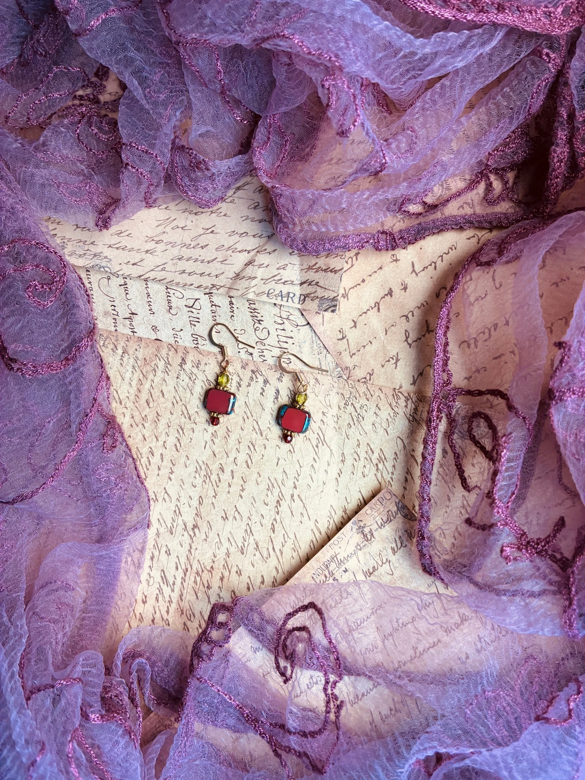 Forbidden Fruit vintage-inspired glass drop earrings displayed against purple fabric.