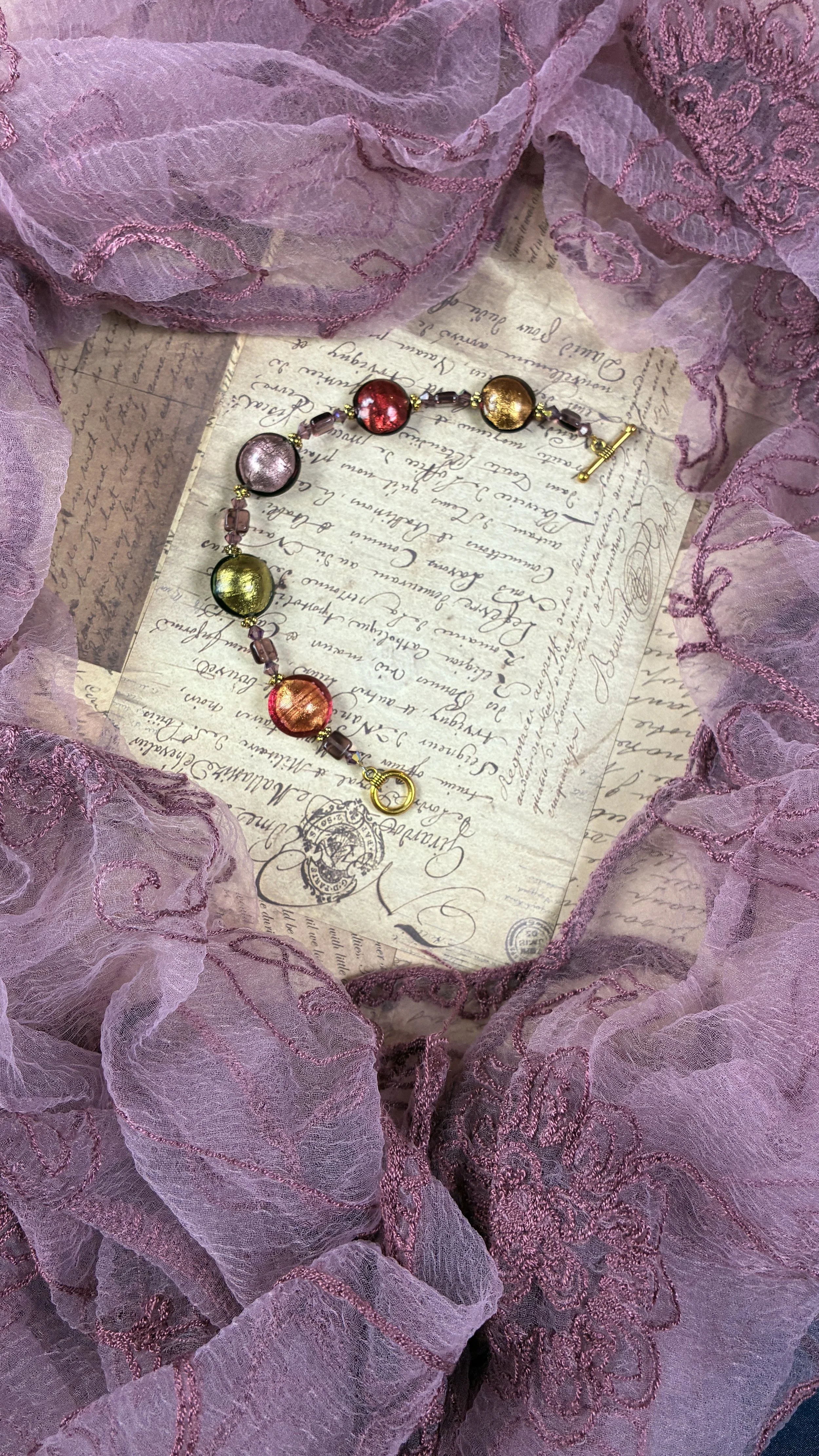 Full Luna bracelet arranged on vintage script paper and framed by a purple embroidered scarf.