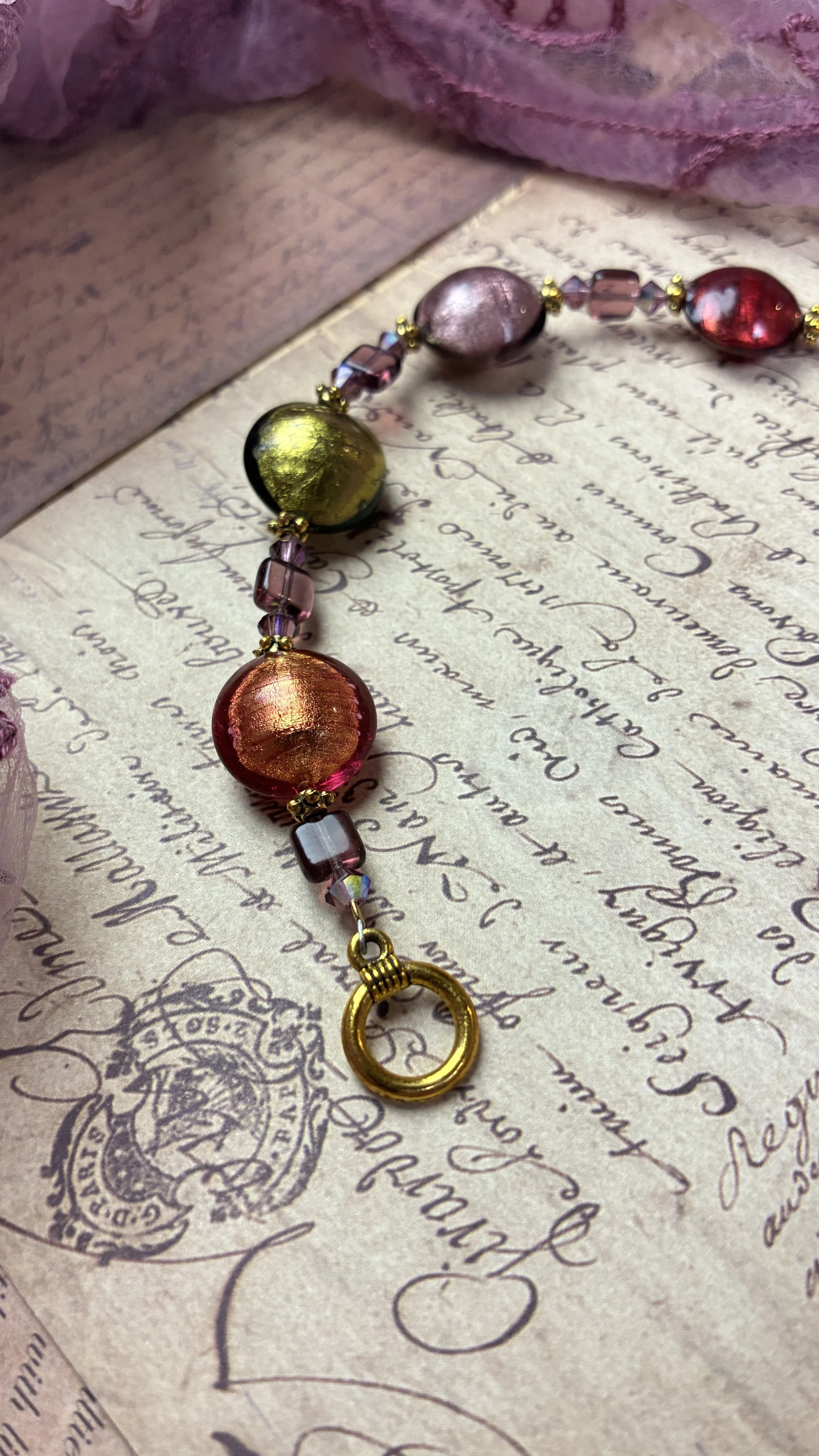 Close-up of Luna’s orange and olive-green foil-glass beads beside the round antique-gold toggle clasp.