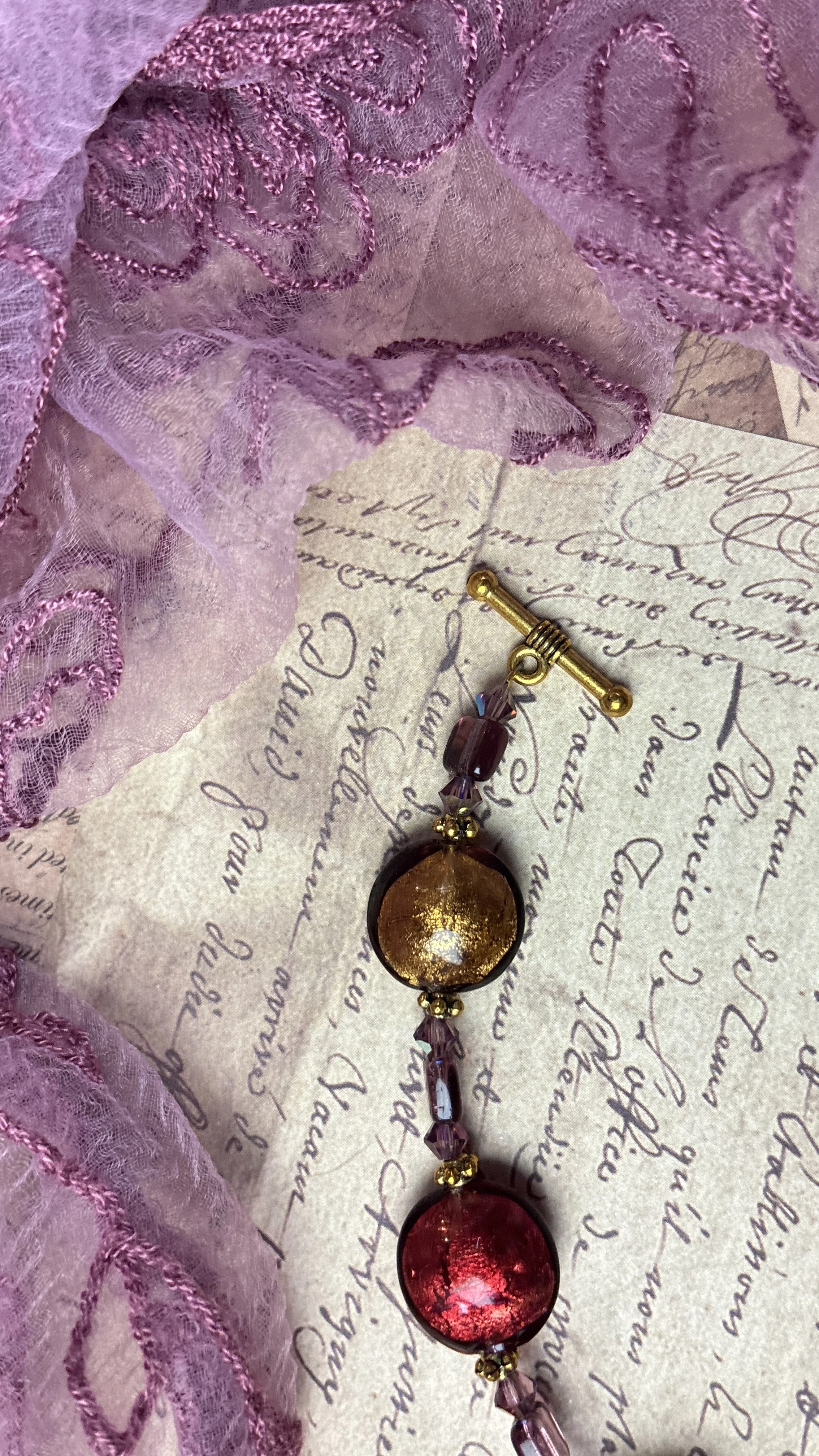 Close-up of Luna’s gold and red foil-glass beads beside the bar end of the antique-gold toggle clasp.