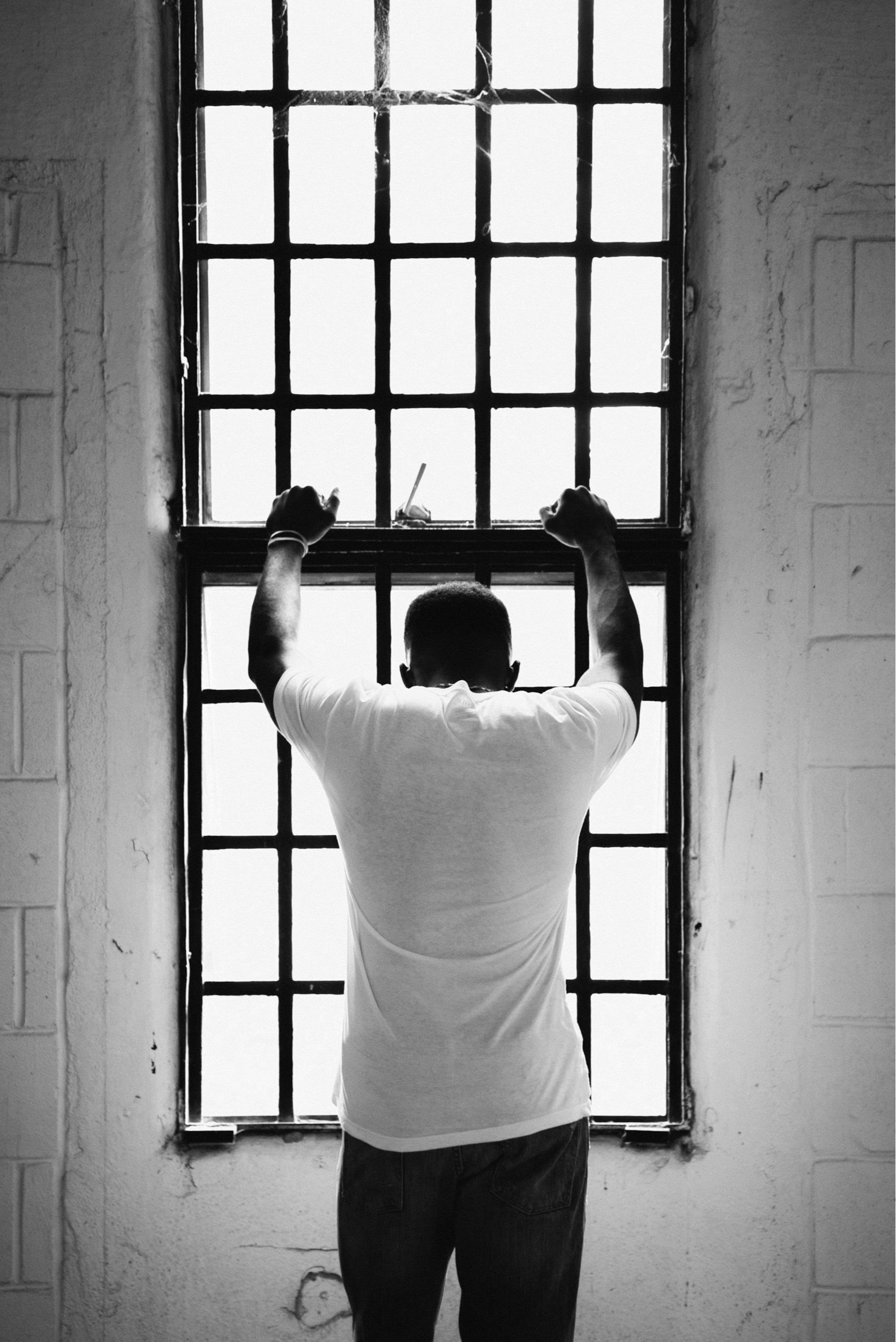 Person standing in front of barred window, holding bars, black and white photo.