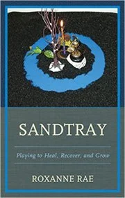 Book cover of 'Sandtray: Playing to Heal, Recover, and Grow' by Roxanne Rae featuring a sandtray with figurines and natural elements on it.