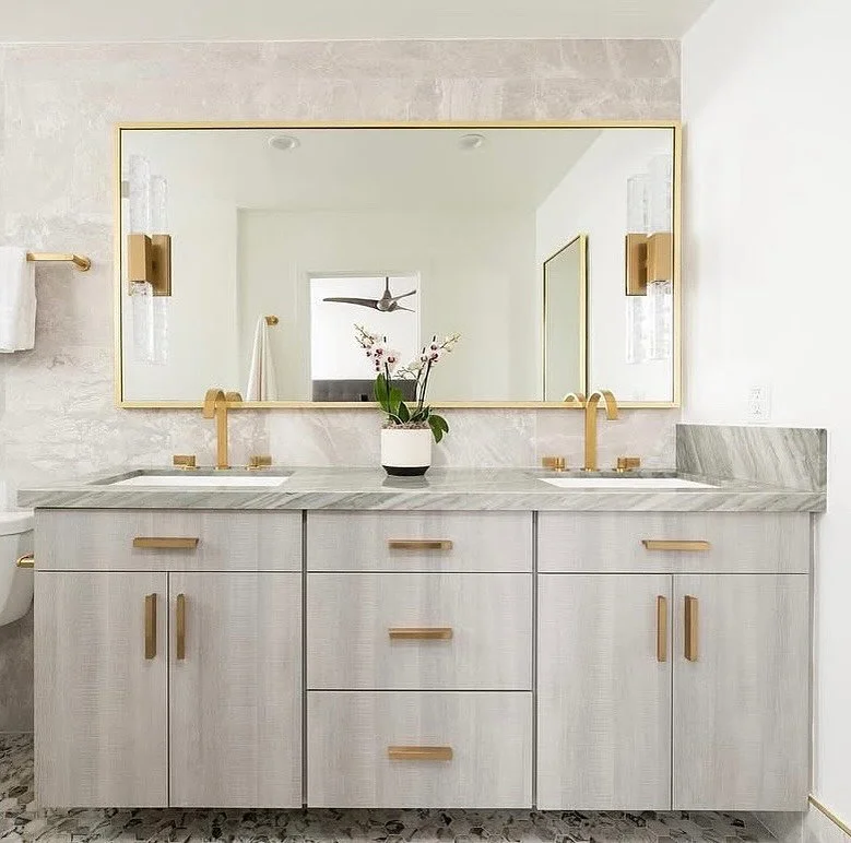 In our clients&rsquo; Newport Beach beach house, this serene primary bath pairs soft gray cabinetry and brass accents with a vein-cut marble countertop for an effortlessly refined look. Every element&mdash;right down to the mirror frame&mdash;was des