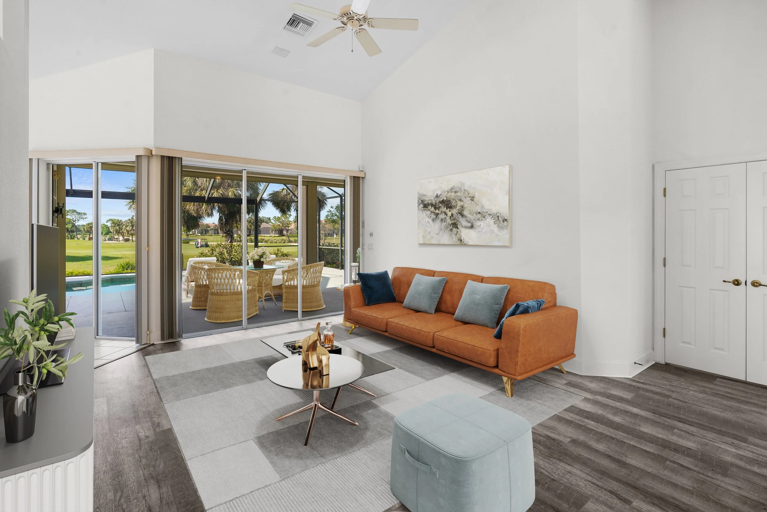 Living room with orange sofa, blue and gray pillows, modern coffee table, large sliding glass doors leading to a patio with outdoor dining, view of a backyard with pool and grass lawn, ceiling fan, painted white walls, and wood flooring.
