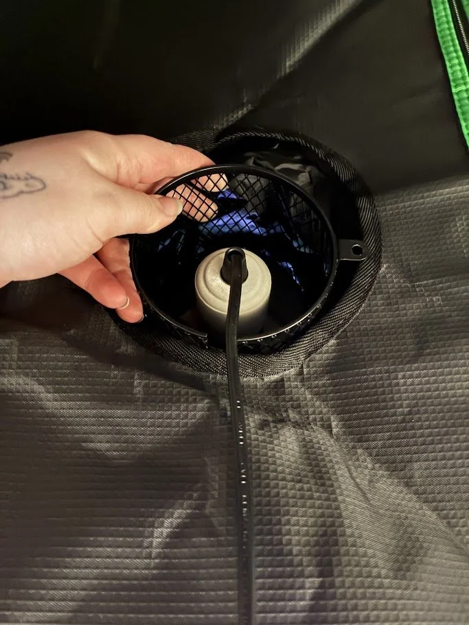 A hand adjusting a camping stove inside a black tent or sleeping bag with a green zipper.