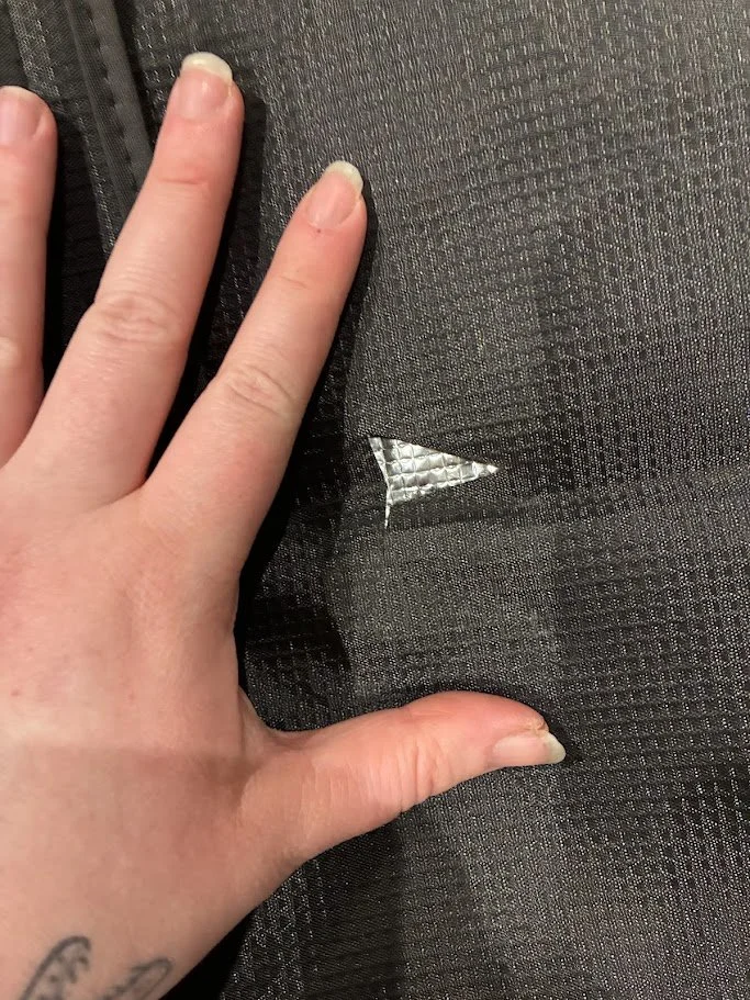 Close-up of a person's hand touching a tear in black fabric, revealing reflective silver lining underneath.