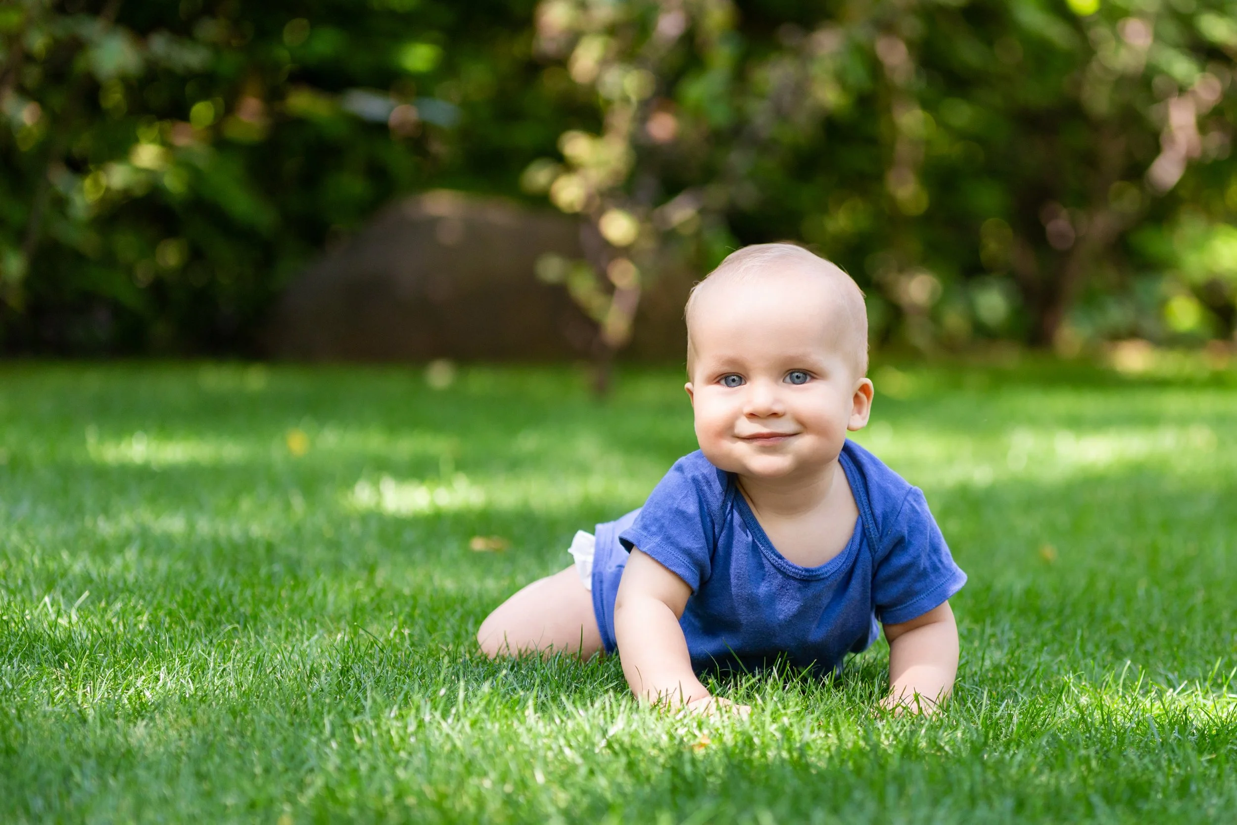 Happy infant in blue onesie crawling on green grass, enjoying outdoor playtime