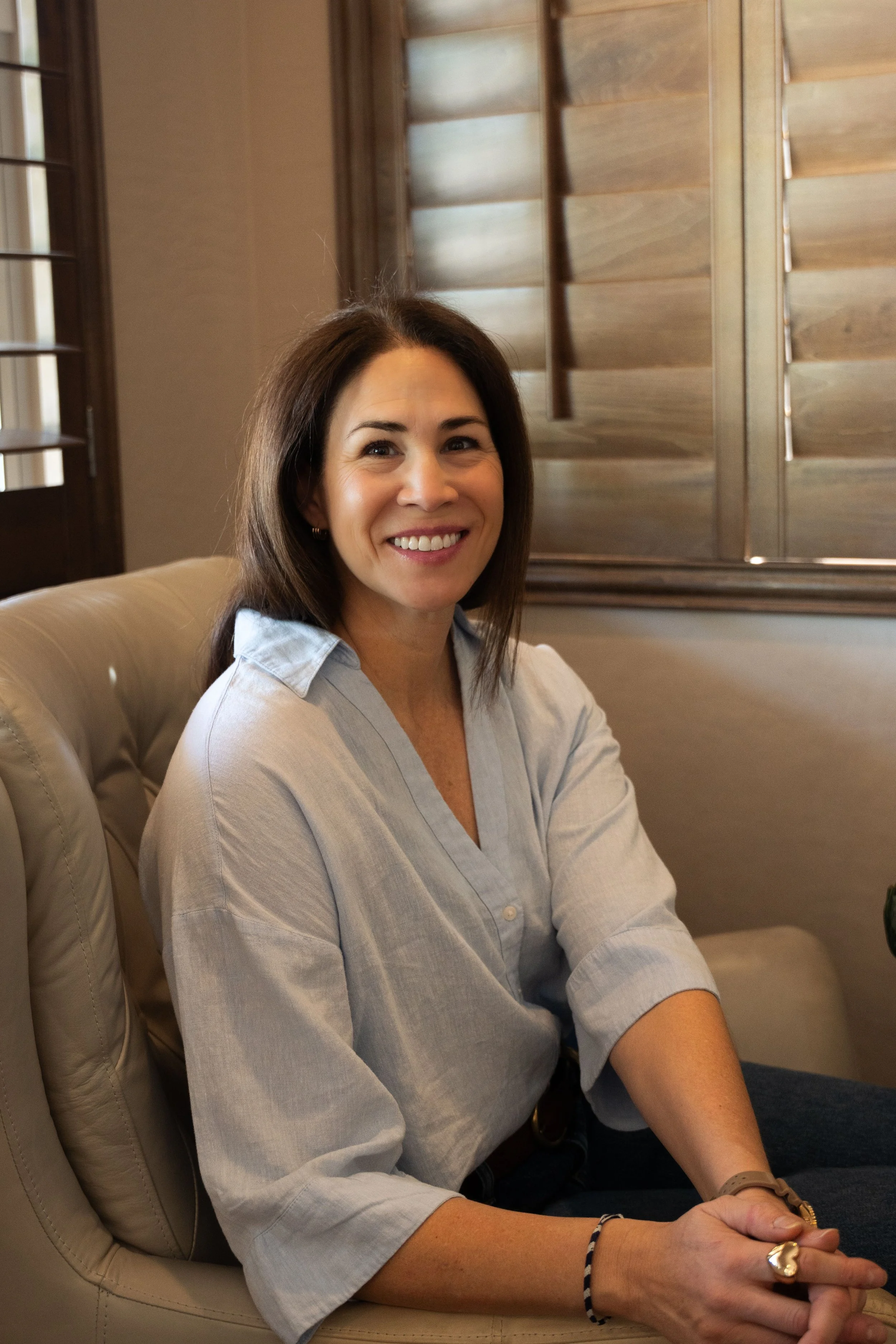 A woman in a blue blouse sitting on a couch, smiling at the camera.