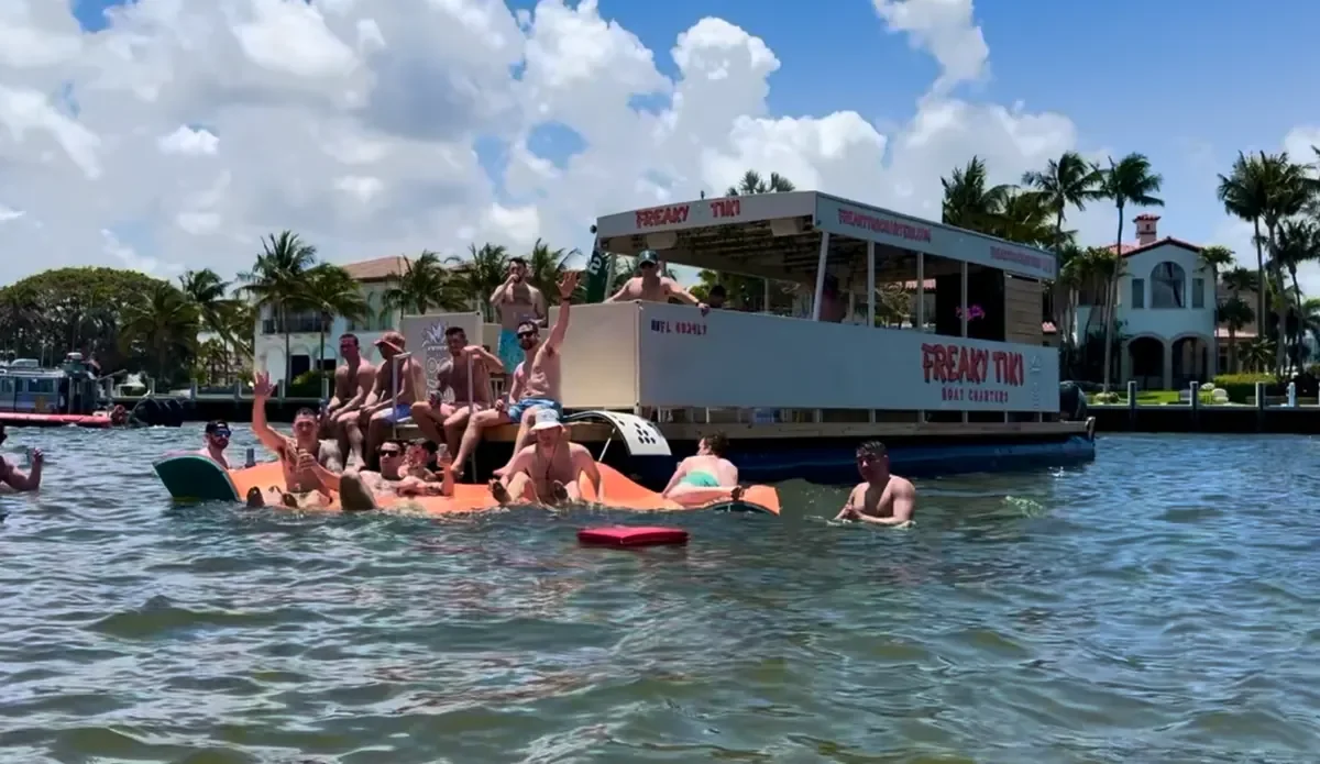 People on at the freaky tiki in Fort Lauderdale with a covered deck, on a body of water, with houses and palm trees in the background.