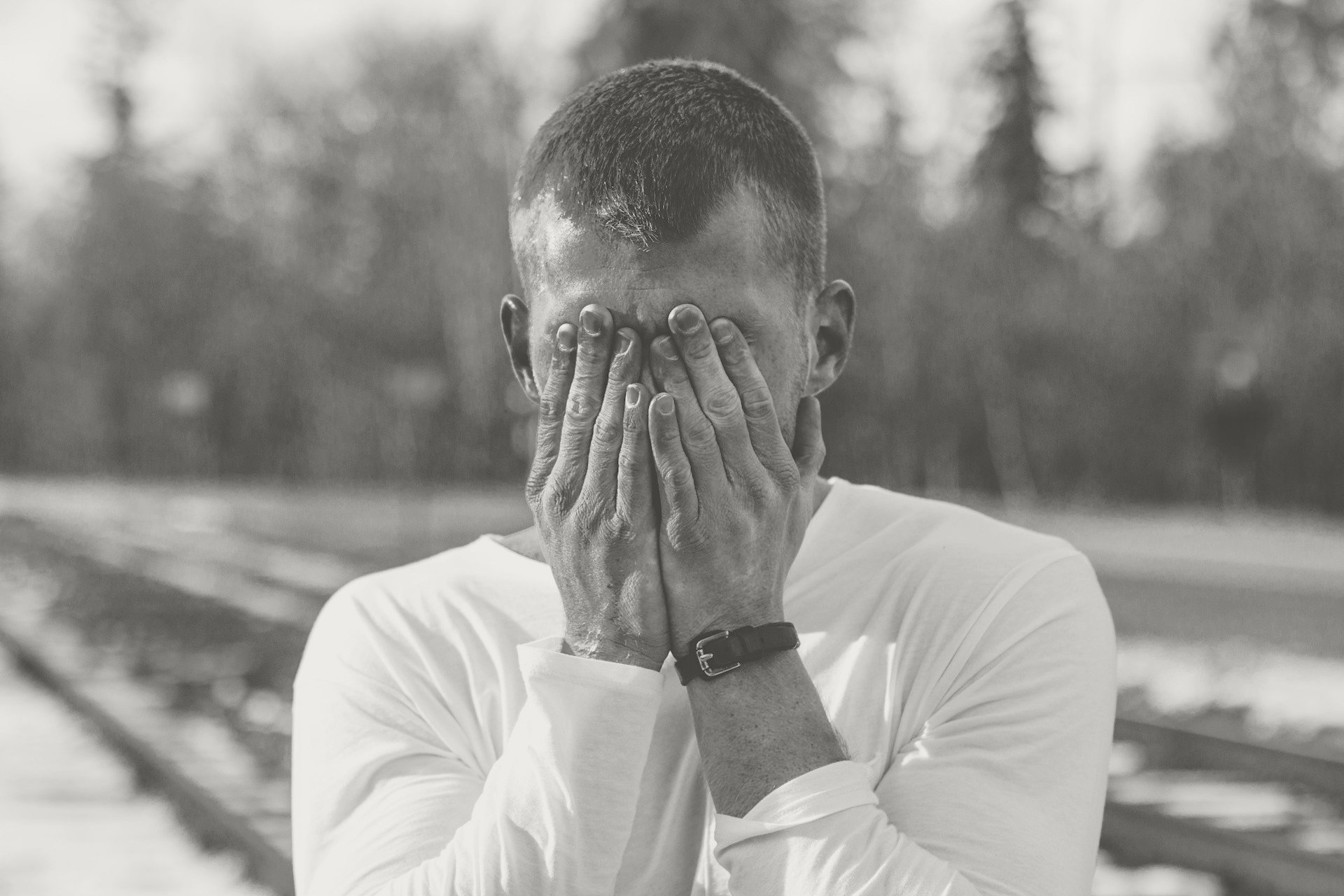 Man covering his face in front of trees and traintracks