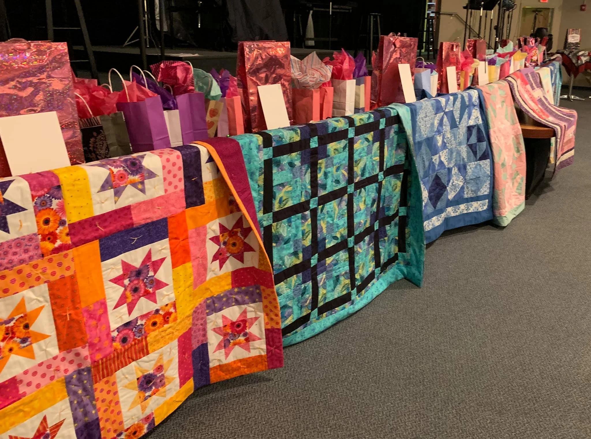 A quilt with various colorful patches, sewing spools, and quilting tools arranged on it, including a pair of red fuzzy scissors, a pattern template, and a rotary cutter.