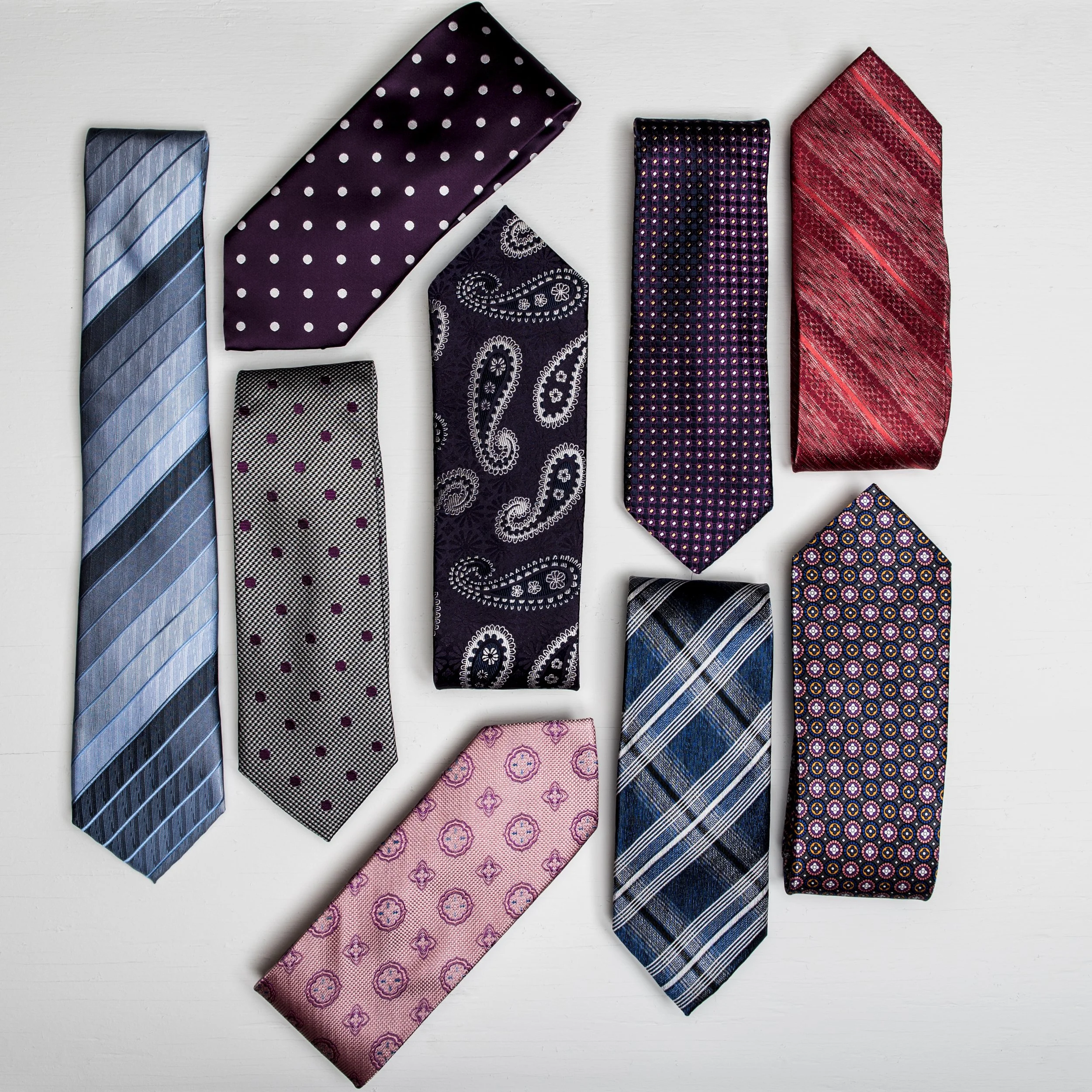 A collection of ten men's neckties with various patterns and colors, arranged on a white surface.
