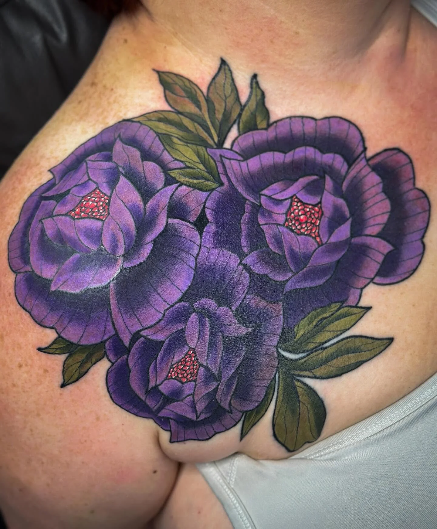 Colorful tattoo of purple flowers with green leaves on a person's shoulder.