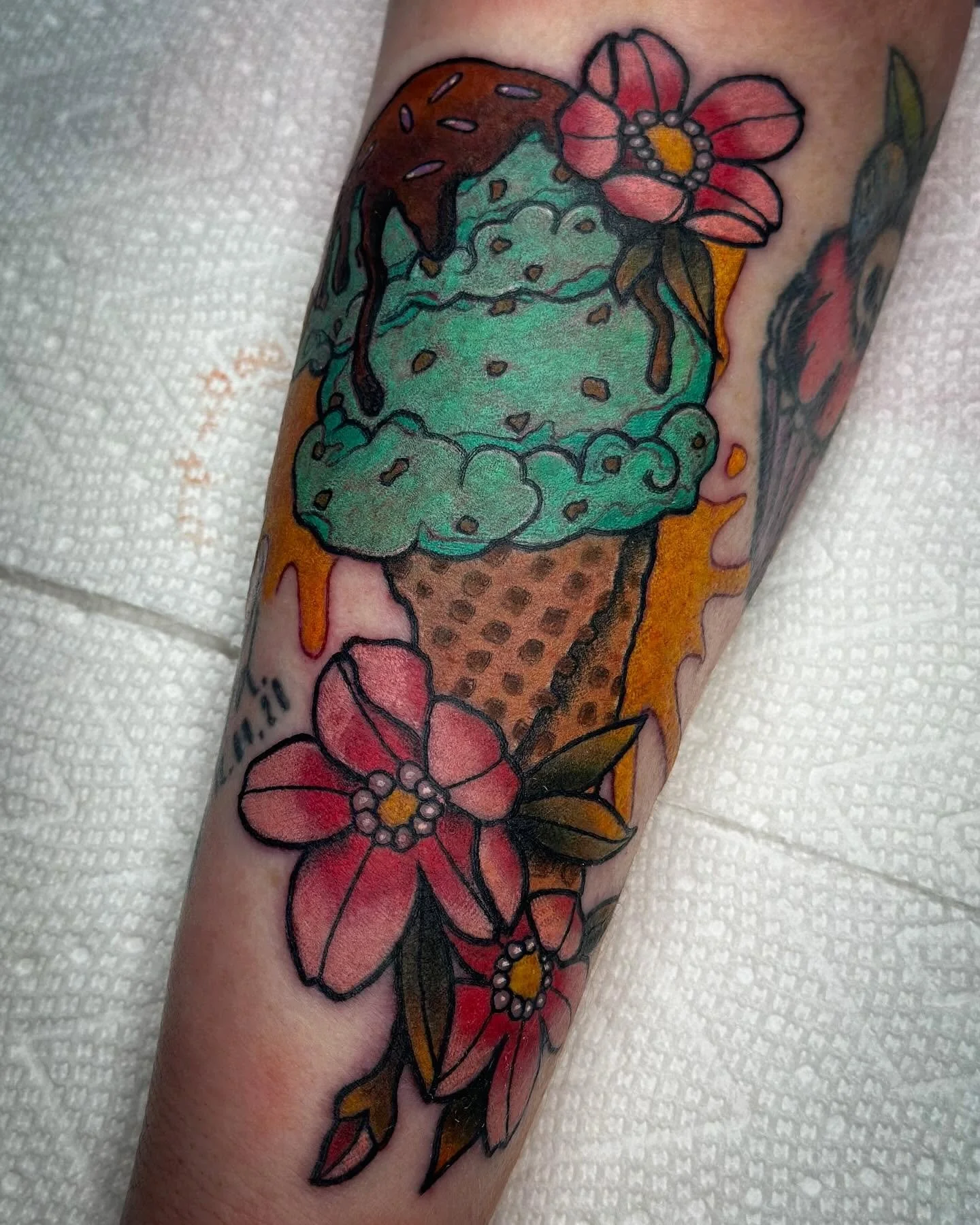 Colorful tattoo of a green ice cream cone with pink and red flowers on the arm.