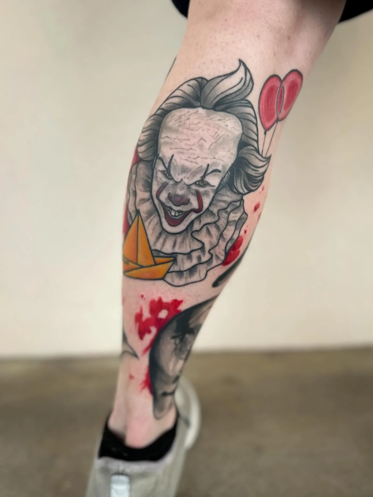 Tattoo of a clown face with red balloons on an arm and leg.