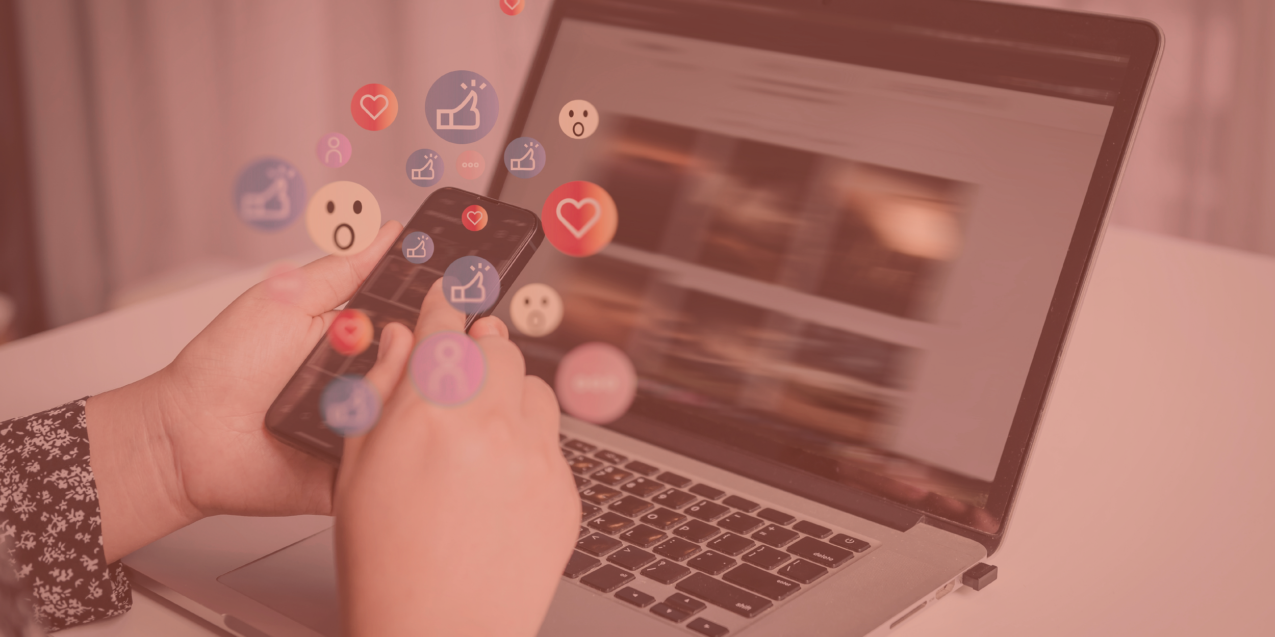 Hand holding phone with emojis and hearts and likes sitting at a desk doing social media