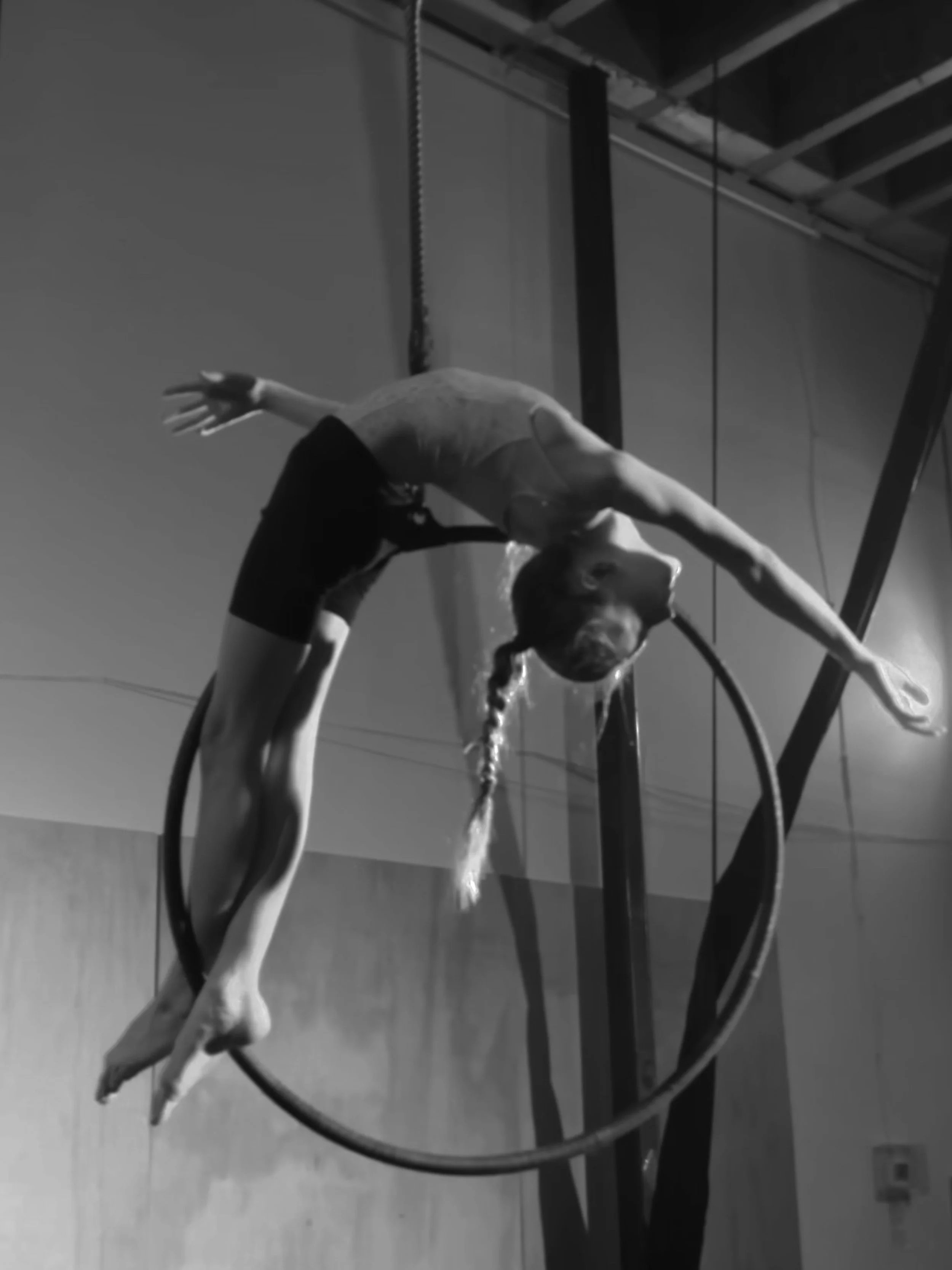 A person with water on their face and hair, bending over a glass table with a circular base, in an industrial-style room with exposed ceiling beams.