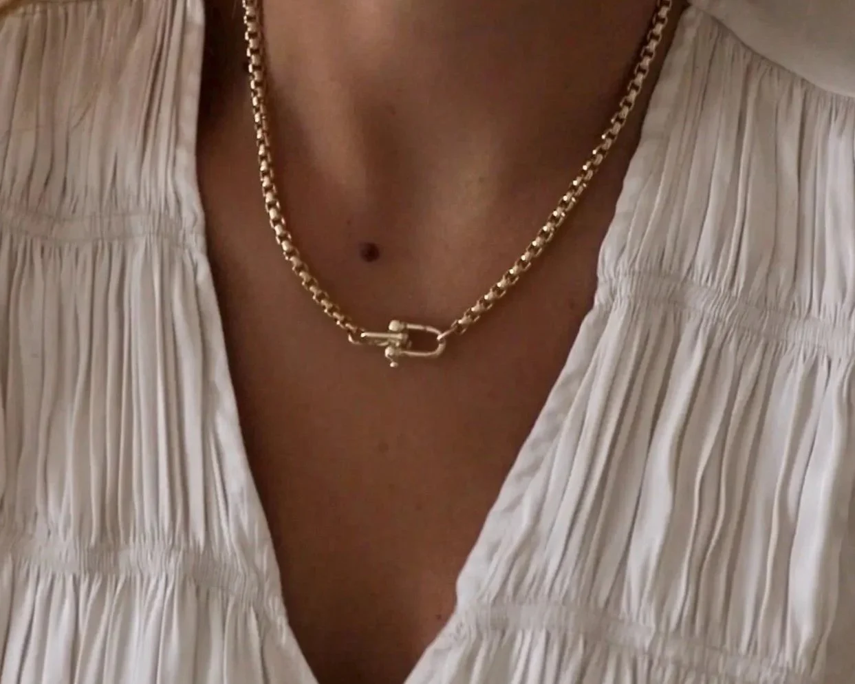 female wearing a cream colored blouse with thier neckline with a gold necklace.