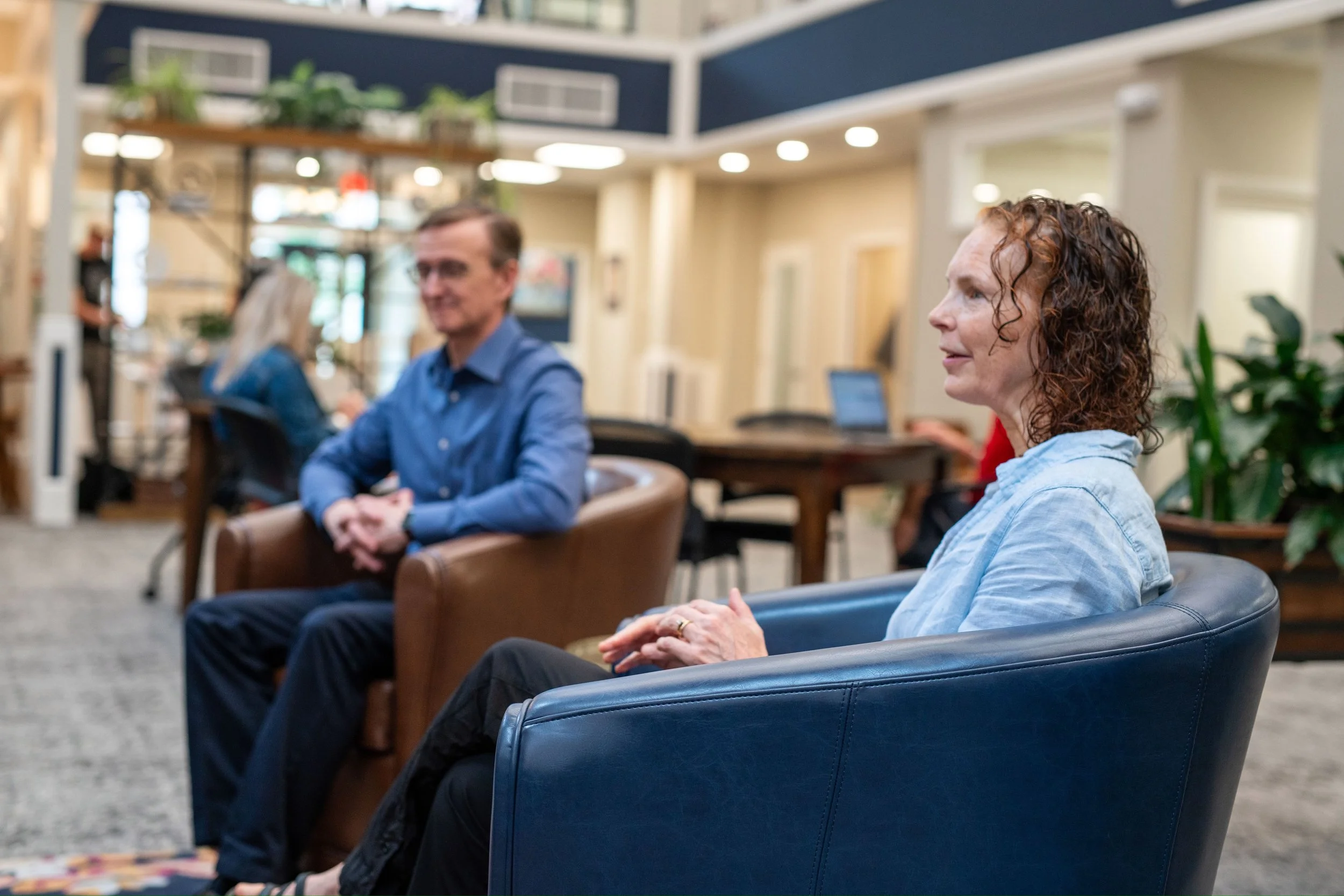 a man and woman are talking while others are working in a coworking space filled with plants and furniture.