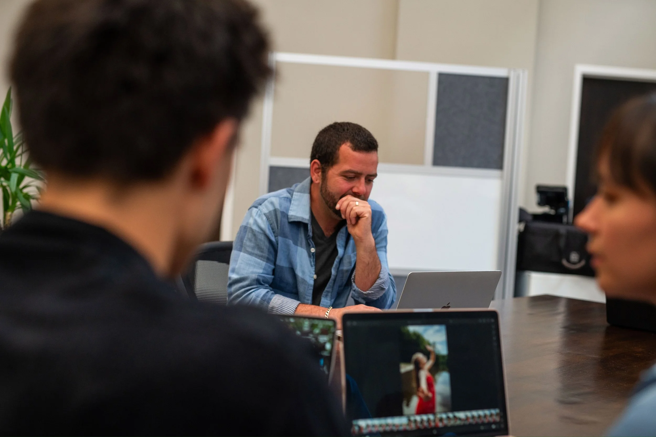 A man sitting at a worktable with another mana nd woman in the foreground. They're cowoking with laptops.