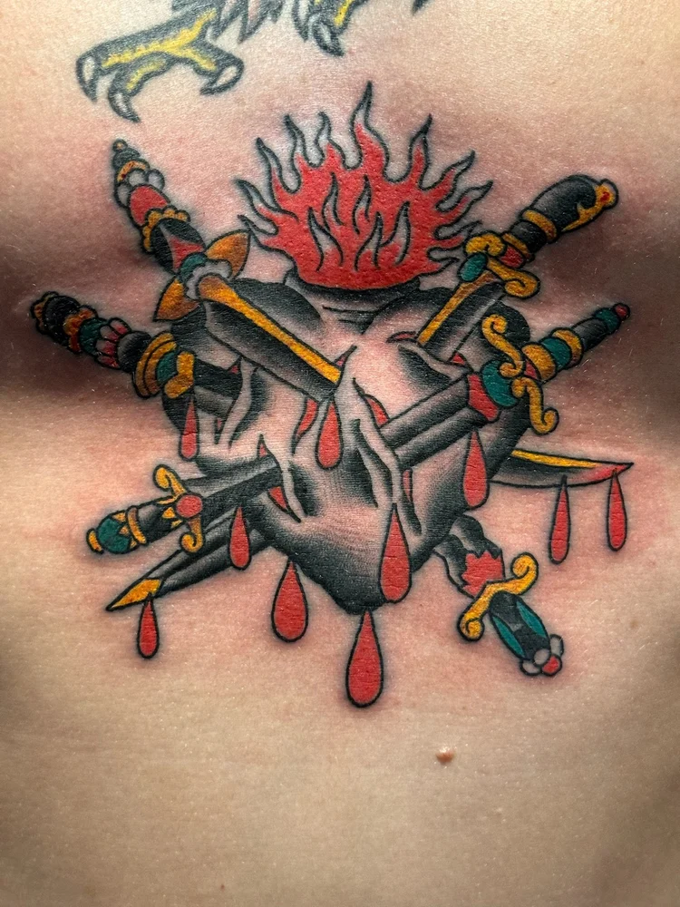 Traditional sacred heart tattoo pierced by swords with flames on the sternum