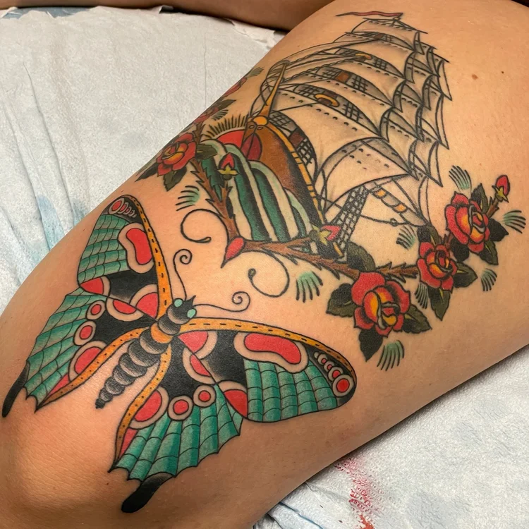 American Traditional butterfly, clipper ship and rose tattoo on the thigh