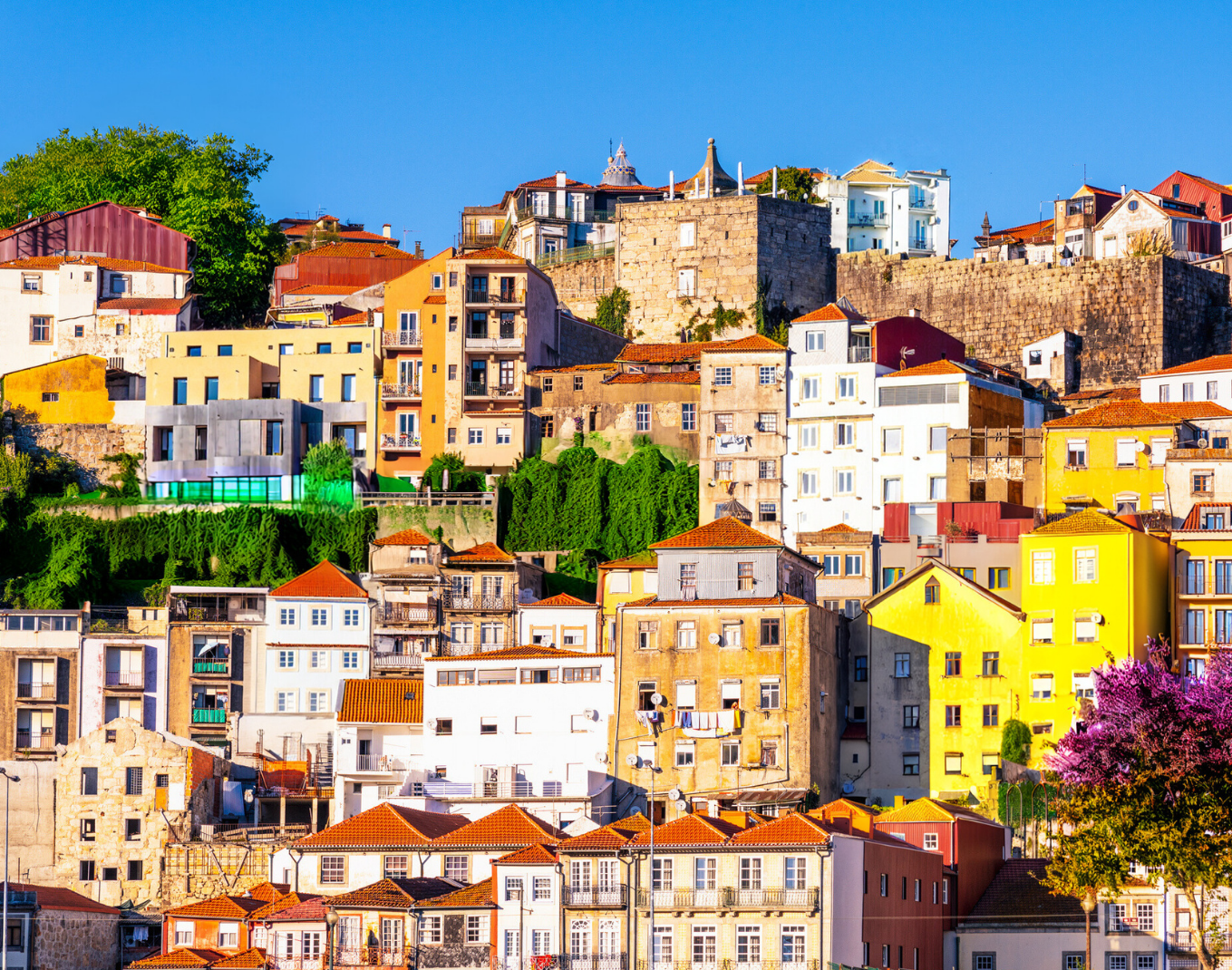 Colorful hillside buildings under a clear blue sky, with some trees and greenery visible.