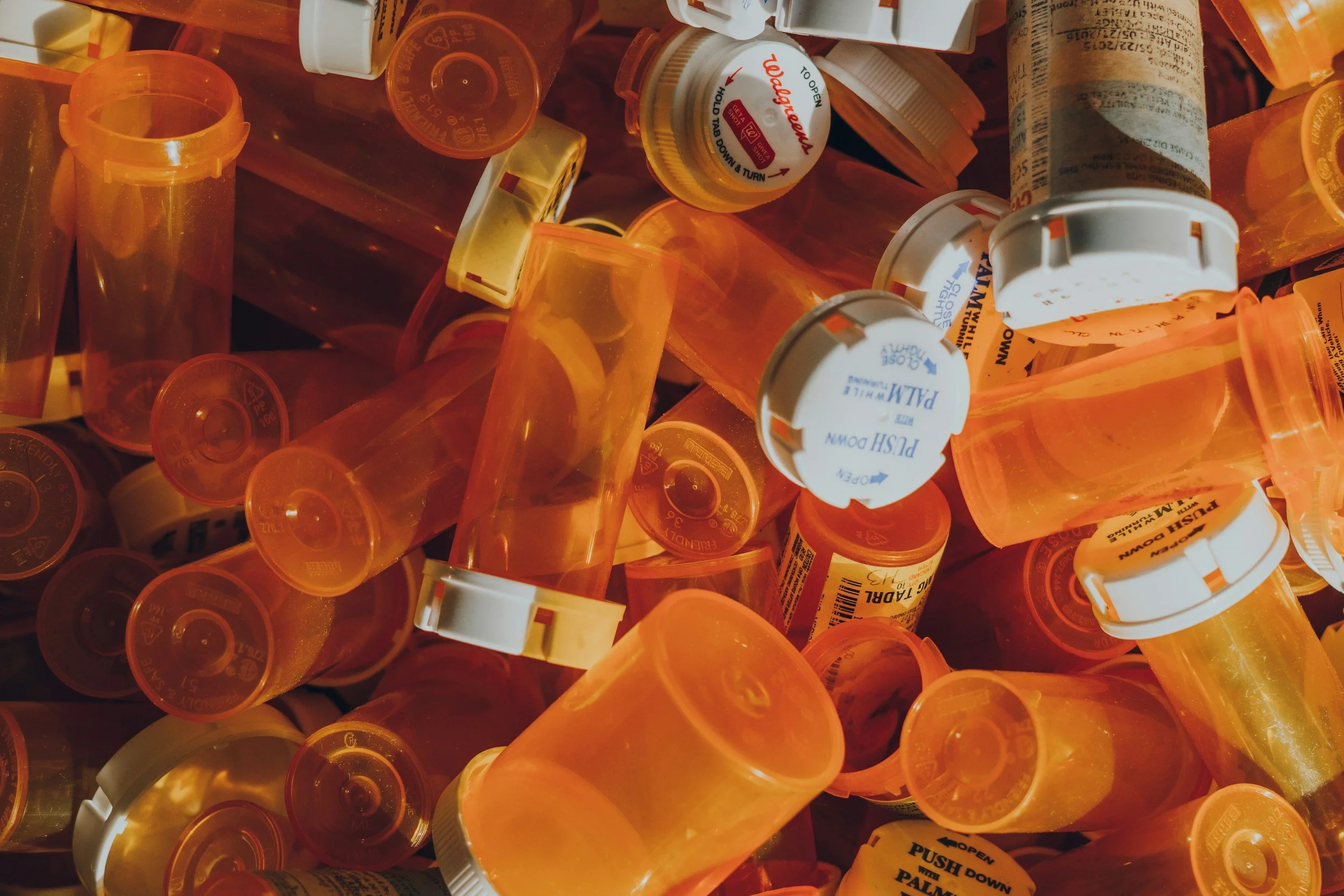 An assortment of orange and white prescription pill bottles, some with labels and caps, piled together.