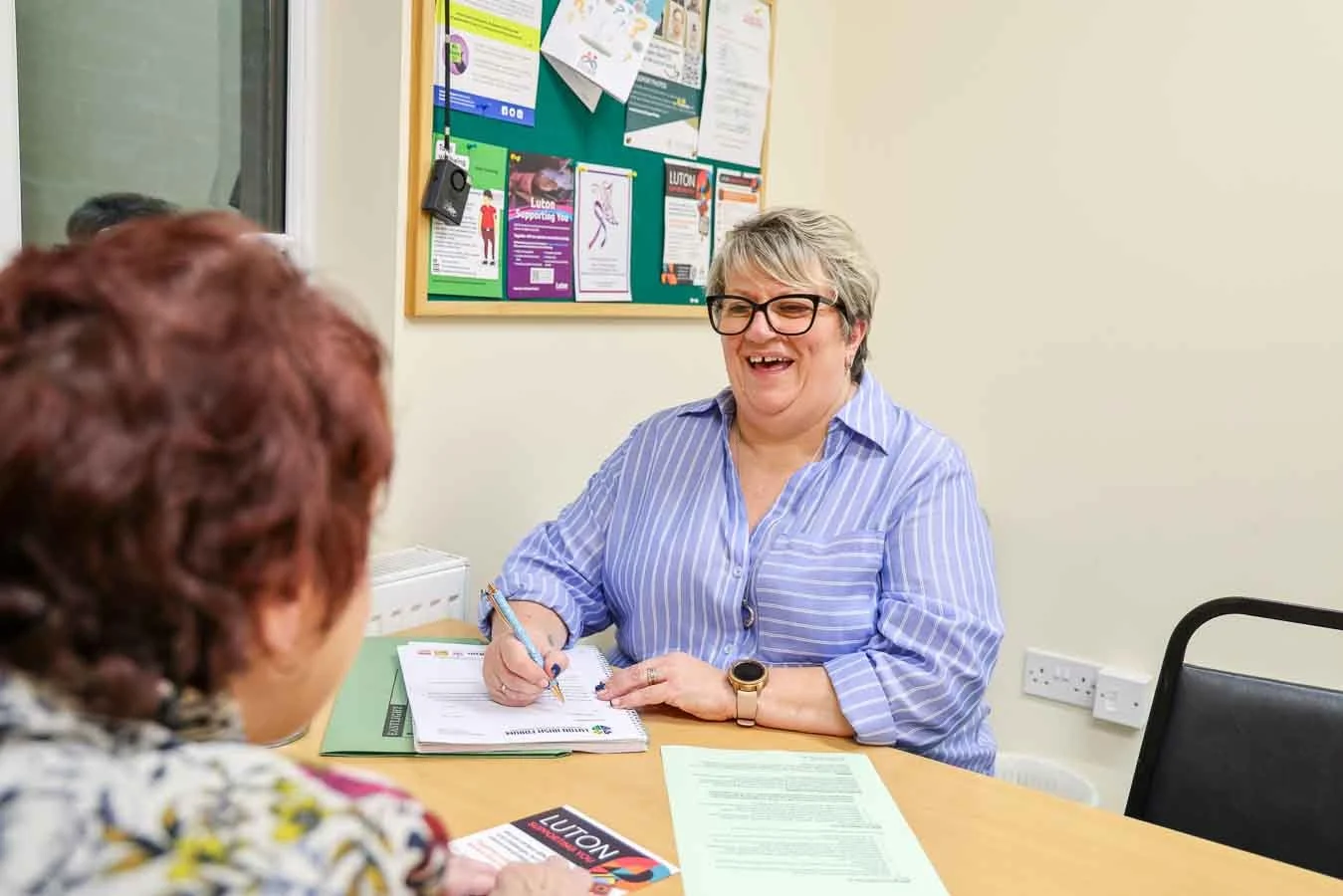 a smiling welfare advisor is helping an elderly Irish female client to apply for benefits