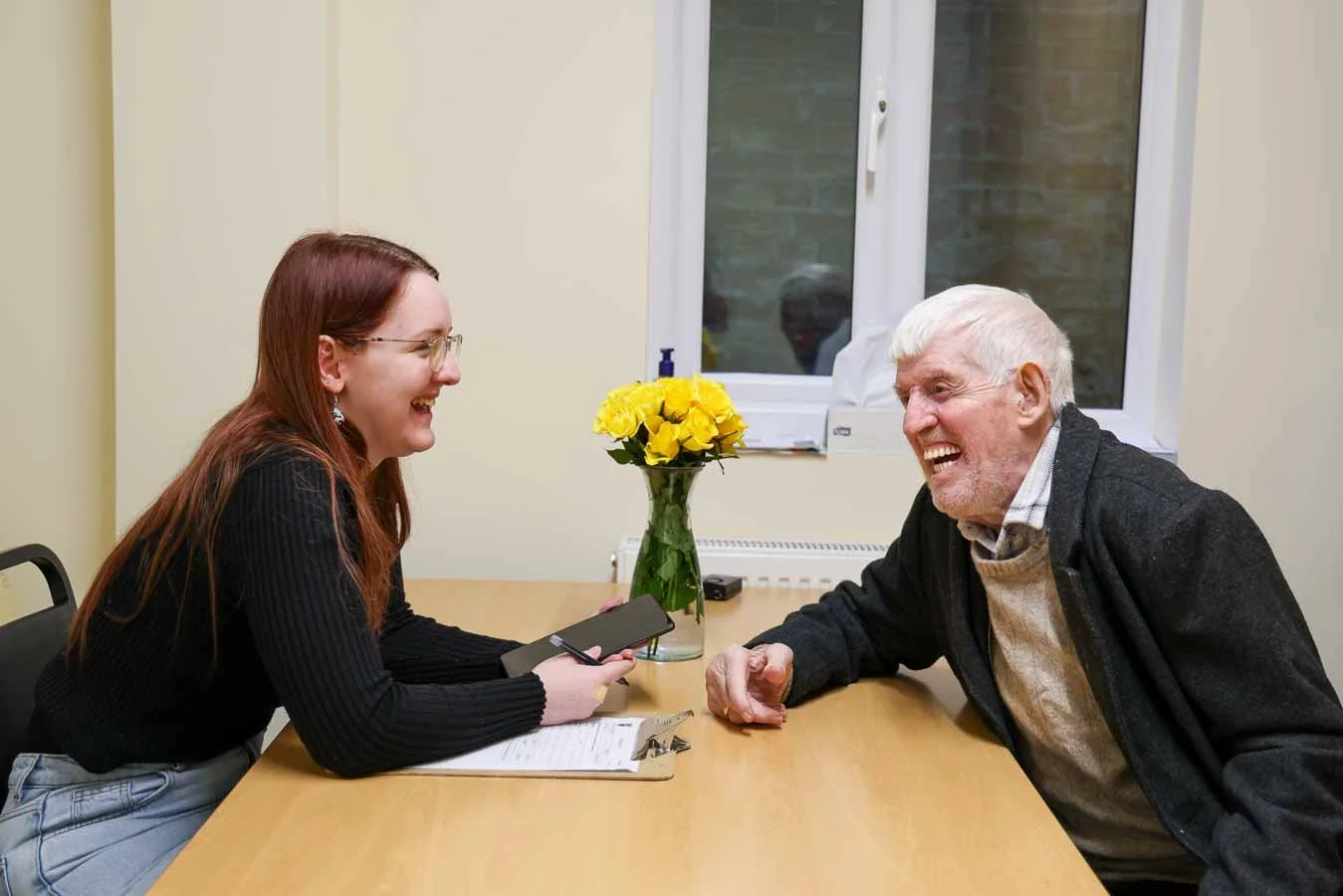 A young woman and an elderly man and talking and smiling. She has helped him complete a welfare form