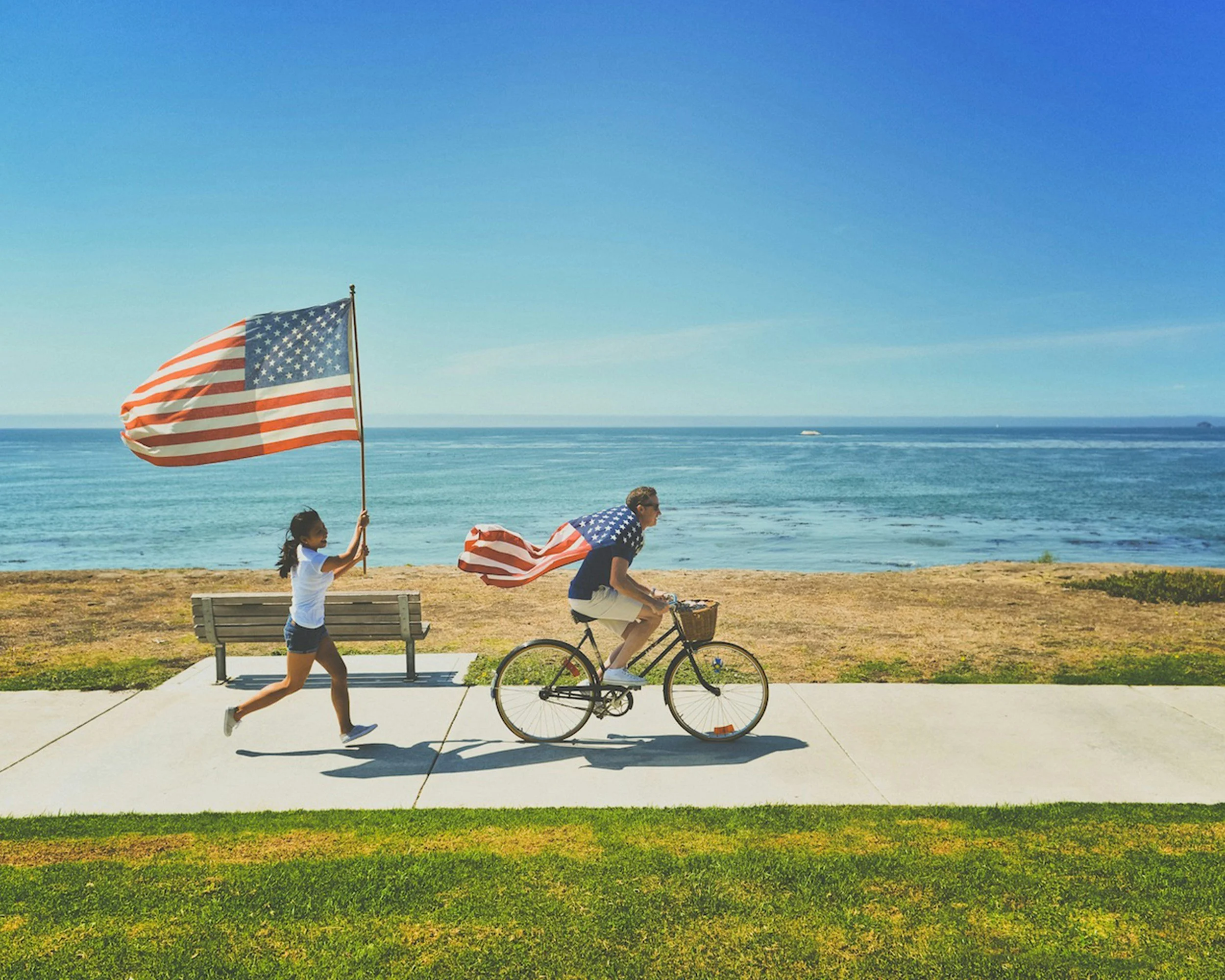 a person riding a bike wearing an American flag as a cape followed by someone running with a flag
