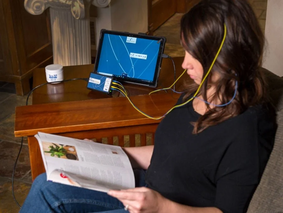 Woman sitting on a couch relaxing and reading while receiving NeuOptimal® neurofeedback.