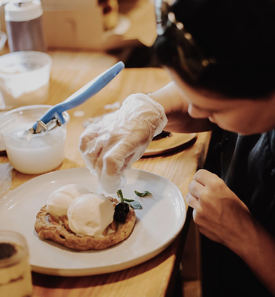 Person decorating a dessert with fresh herbs at a wooden table.
