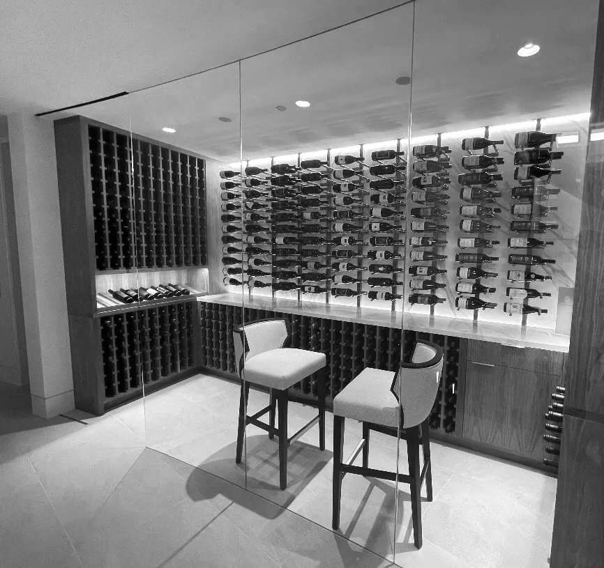 Wine storage room with multiple bottles on horizontal racks, two chairs, and a mirrored wall.