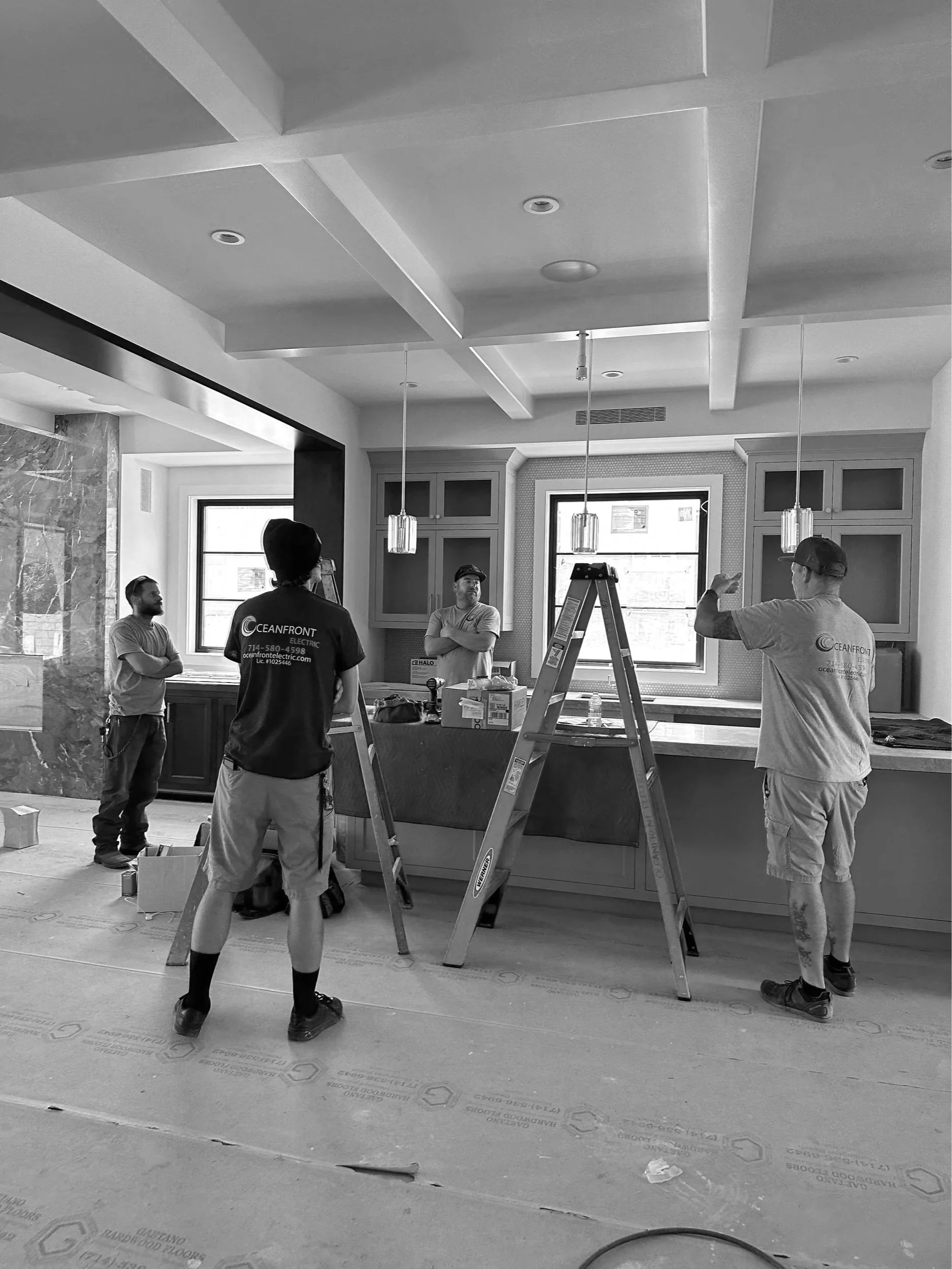 Construction workers working in a kitchen area, with a ladder and tools, discussing tasks. Black and white photo.
