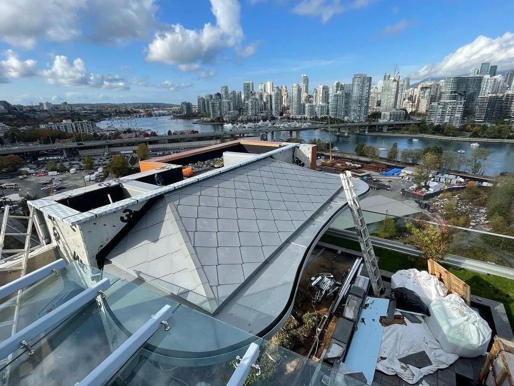 View from a rooftop building under construction, overlooking a city skyline with high-rise buildings, a river, and boats on a cloudy day.