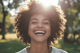 A woman with curly hair smiling in a park during daytime.