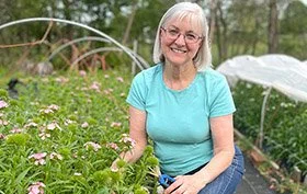 Woman in a garden with flowers, wearing blue t-shirt