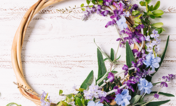 A wreath made of purple and blue flowers on a white wooden background.