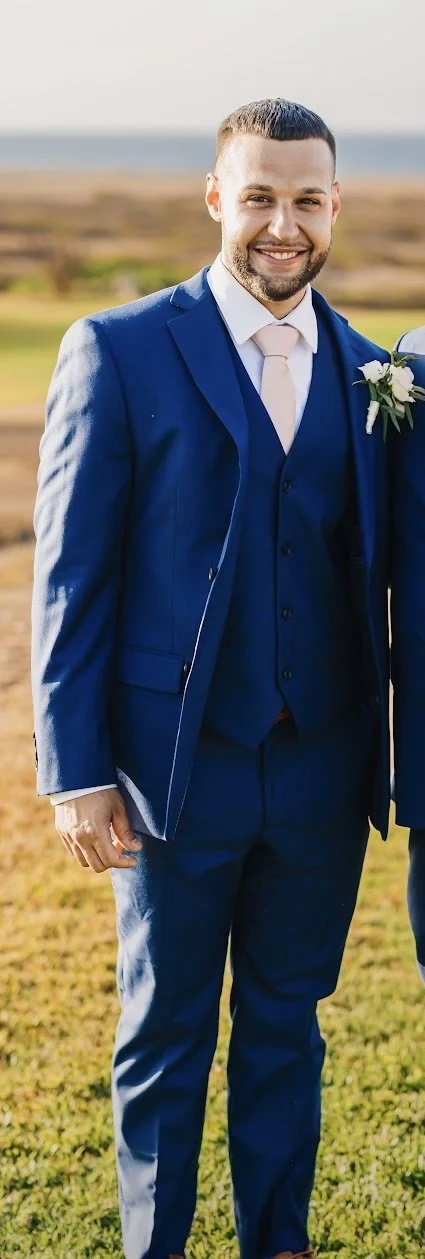 Portrait of a man with short hair and a beard, wearing a blue collared shirt, set against a blue background.