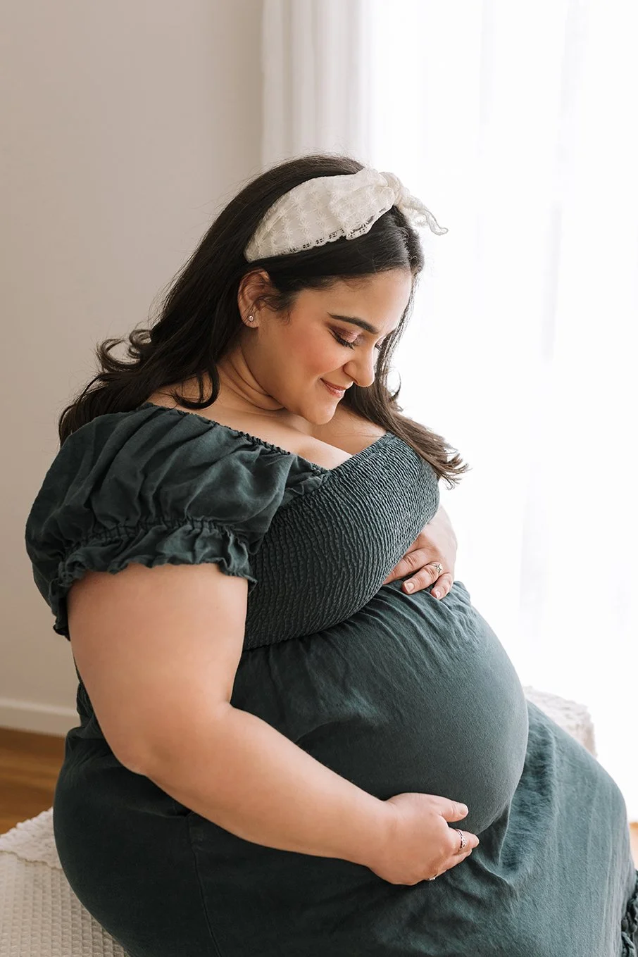 Expectant mother sitting in a neutral-toned photography studio