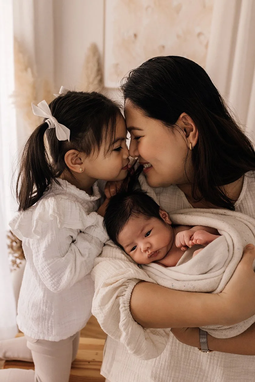 Mother and daughter touching noses while cradling newborn baby in their arms