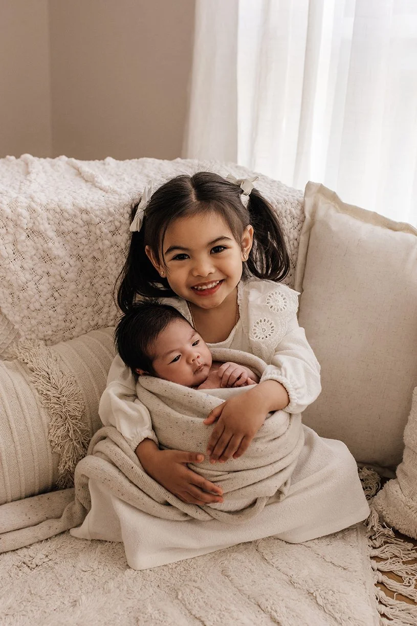 Sister holding her newborn sibling during a family photography session.