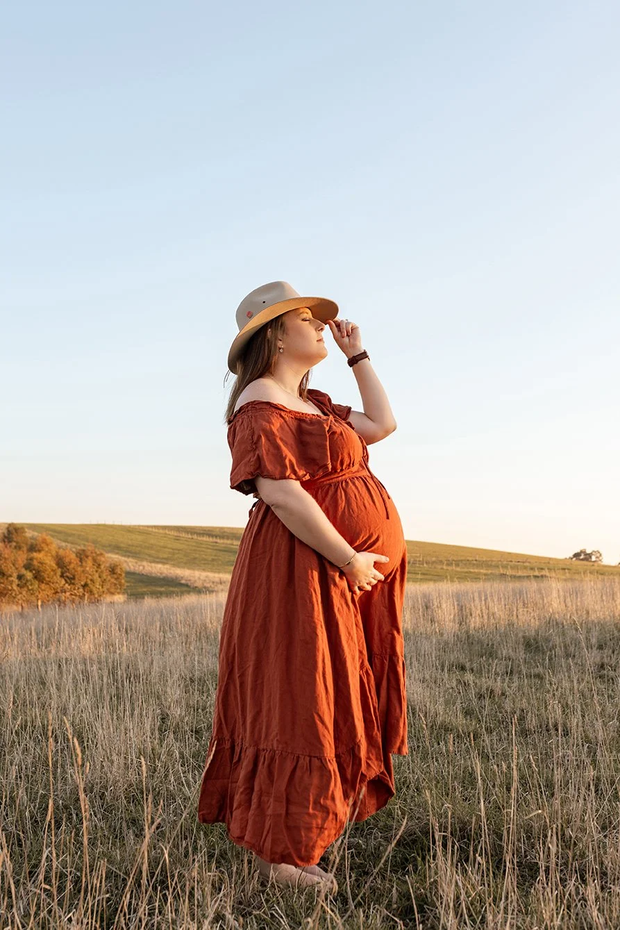 Mother-to-be standing among native grasses at sunset.